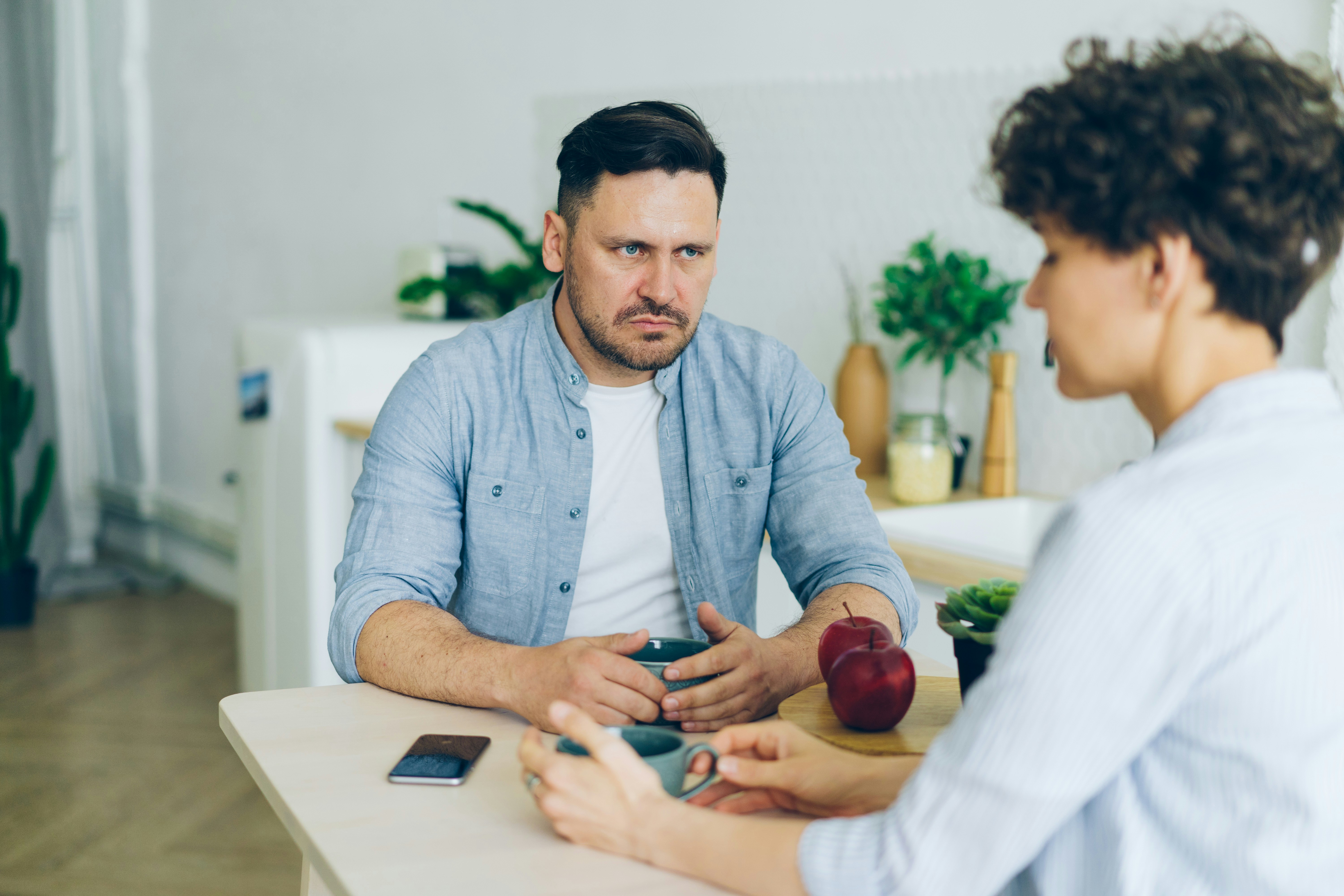 Woman holding wedding ring, man blurred in background, likely in a divorce setting.