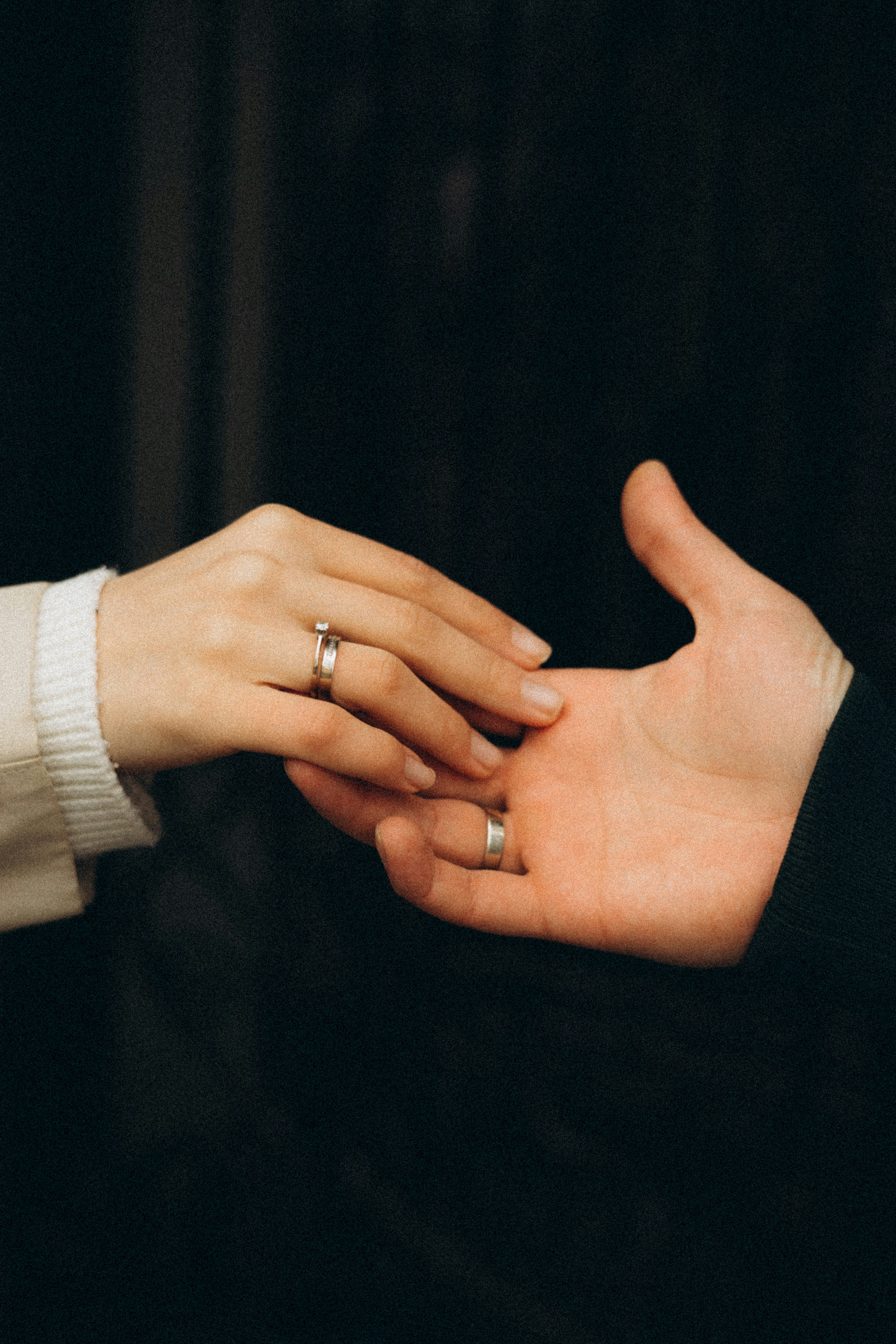 Woman holding wedding ring, man blurred in background, likely in a divorce setting.
