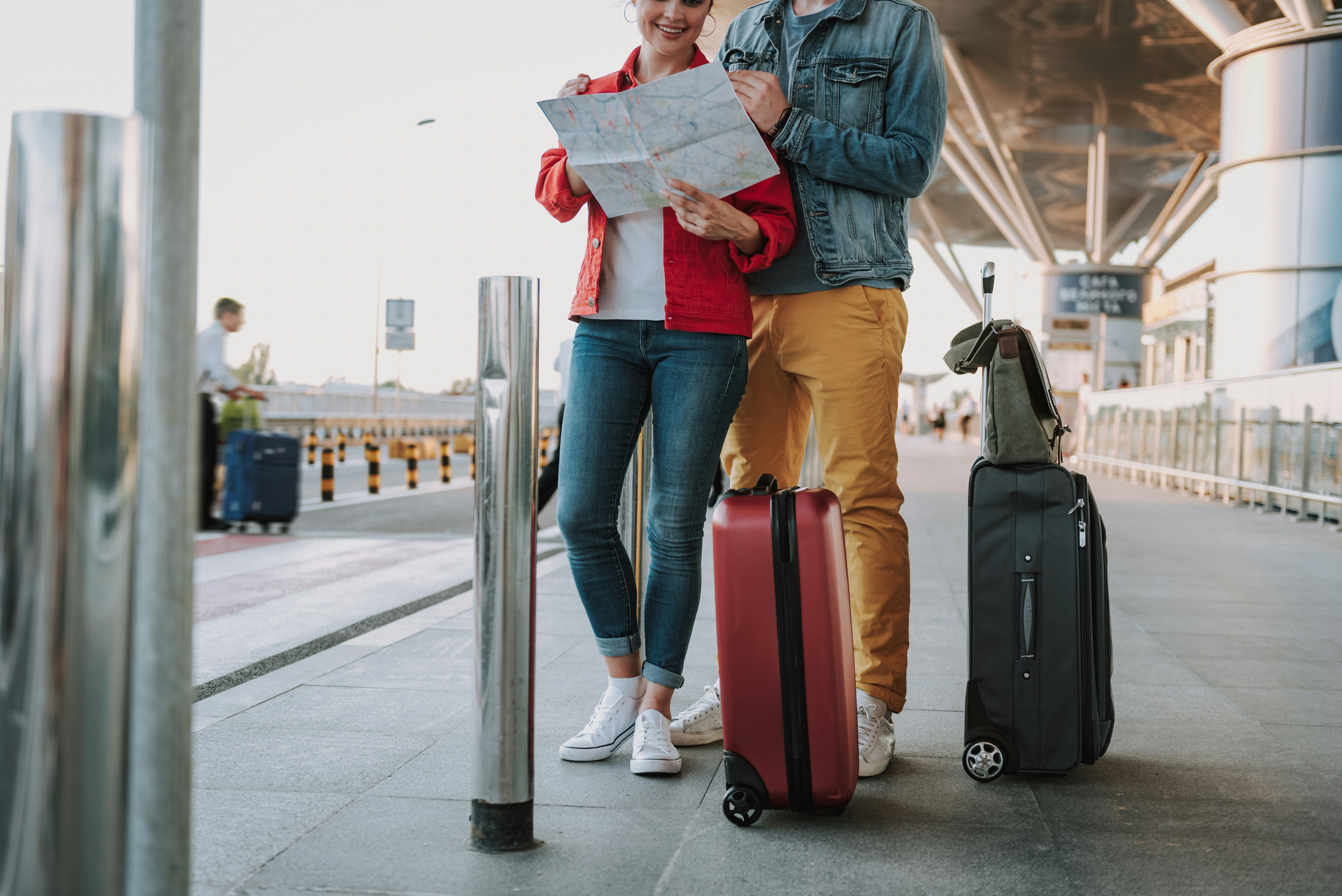 Couple with suitcases looking at a map outside an airport terminal