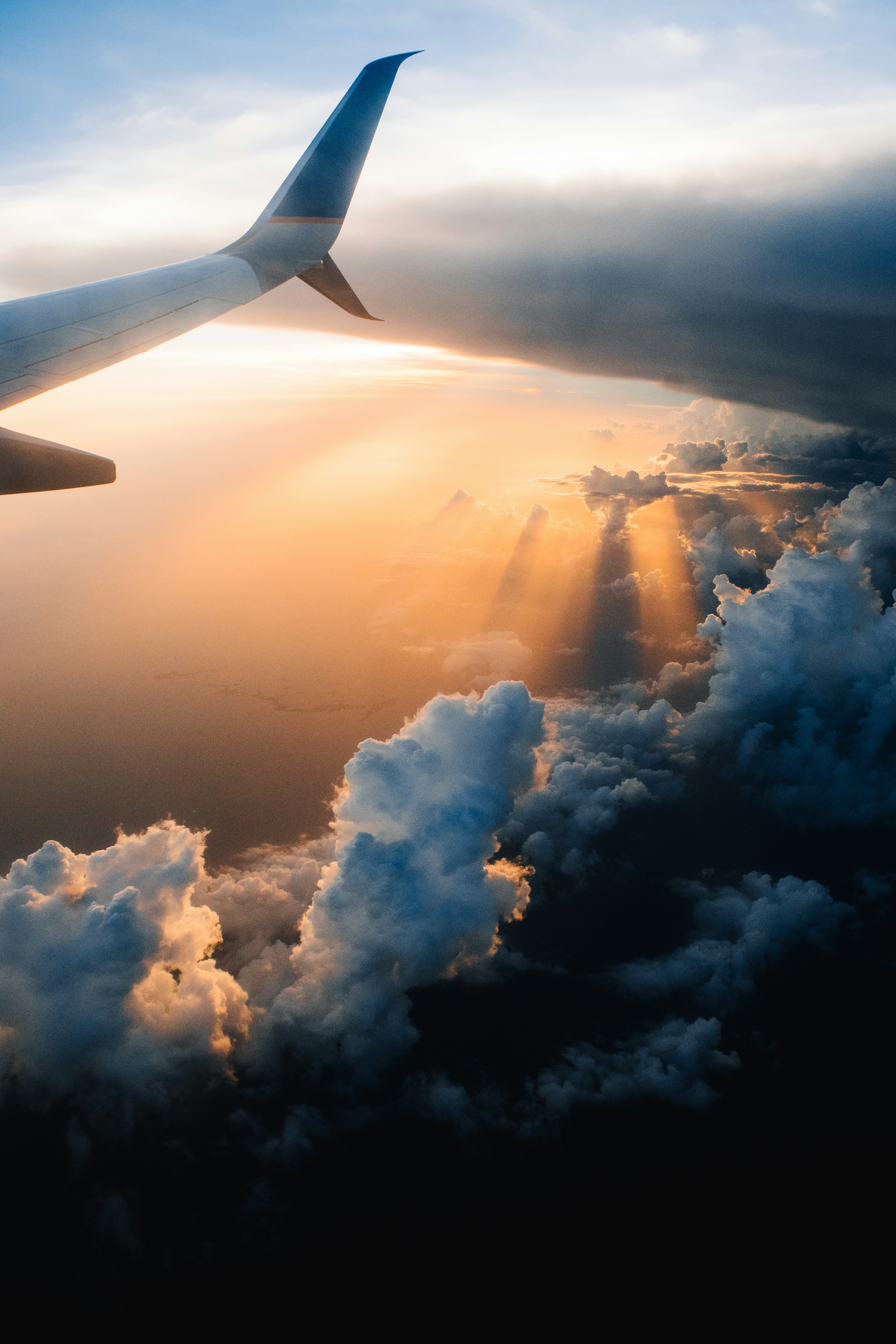 Airplane wing flying above clouds during sunset