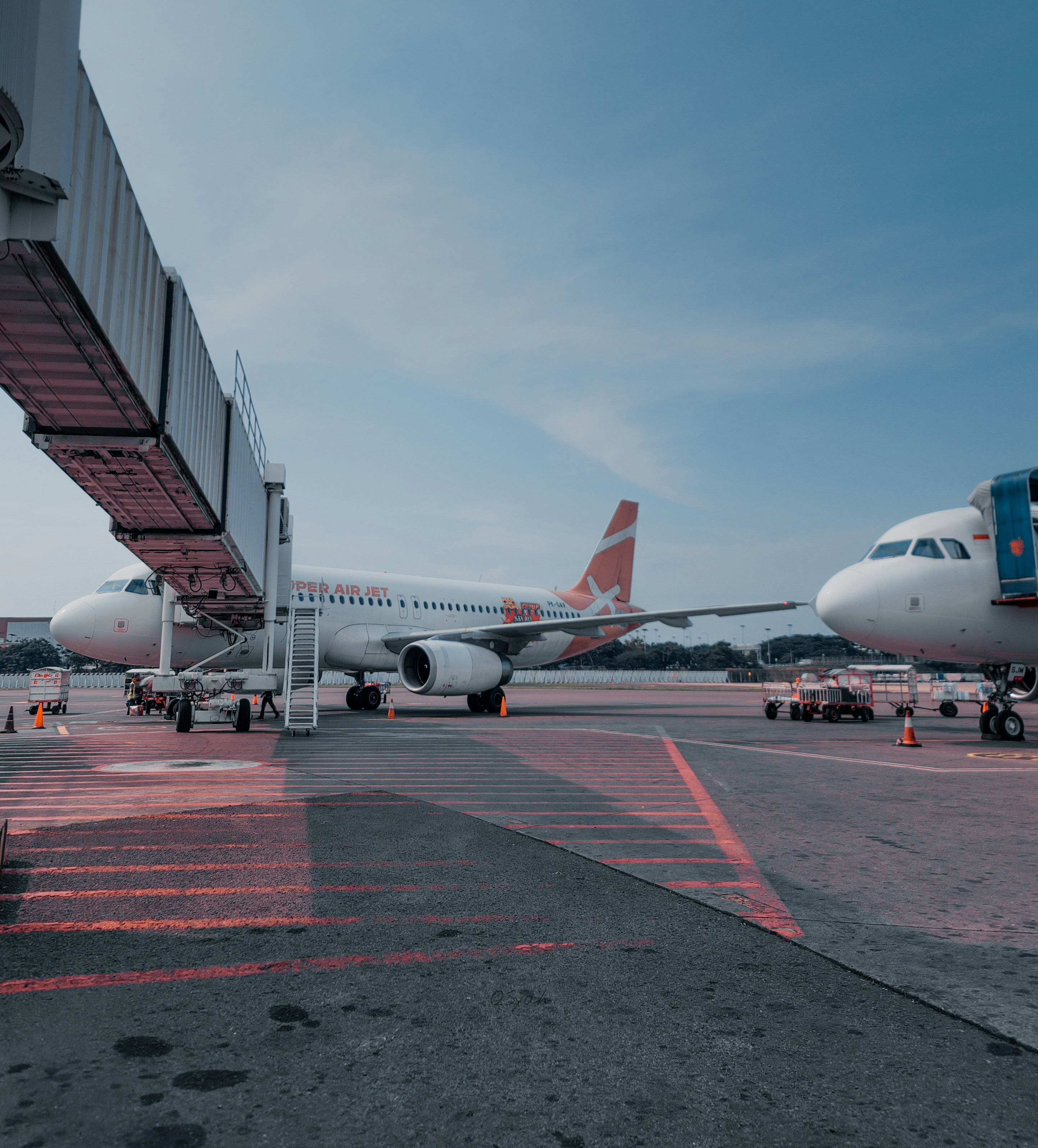 Two airplanes parked at an airport gate with a boarding bridge.