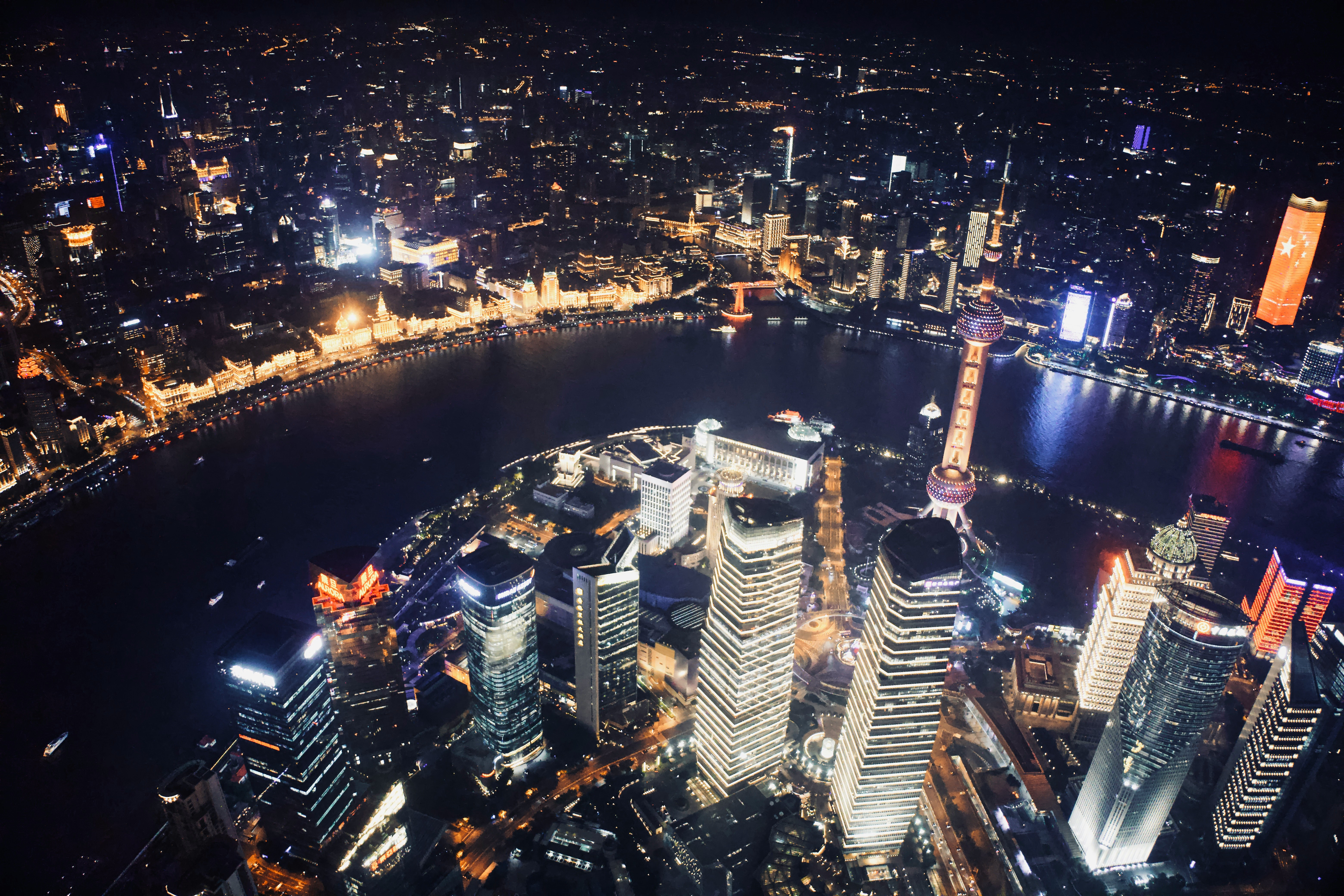 Aerial view of a city skyline at night with illuminated skyscrapers and a river.