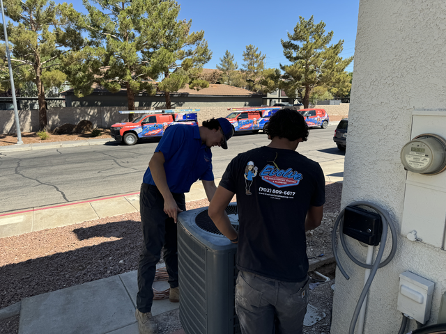 Two technicians working on an outdoor air conditioning unit in a residential area.