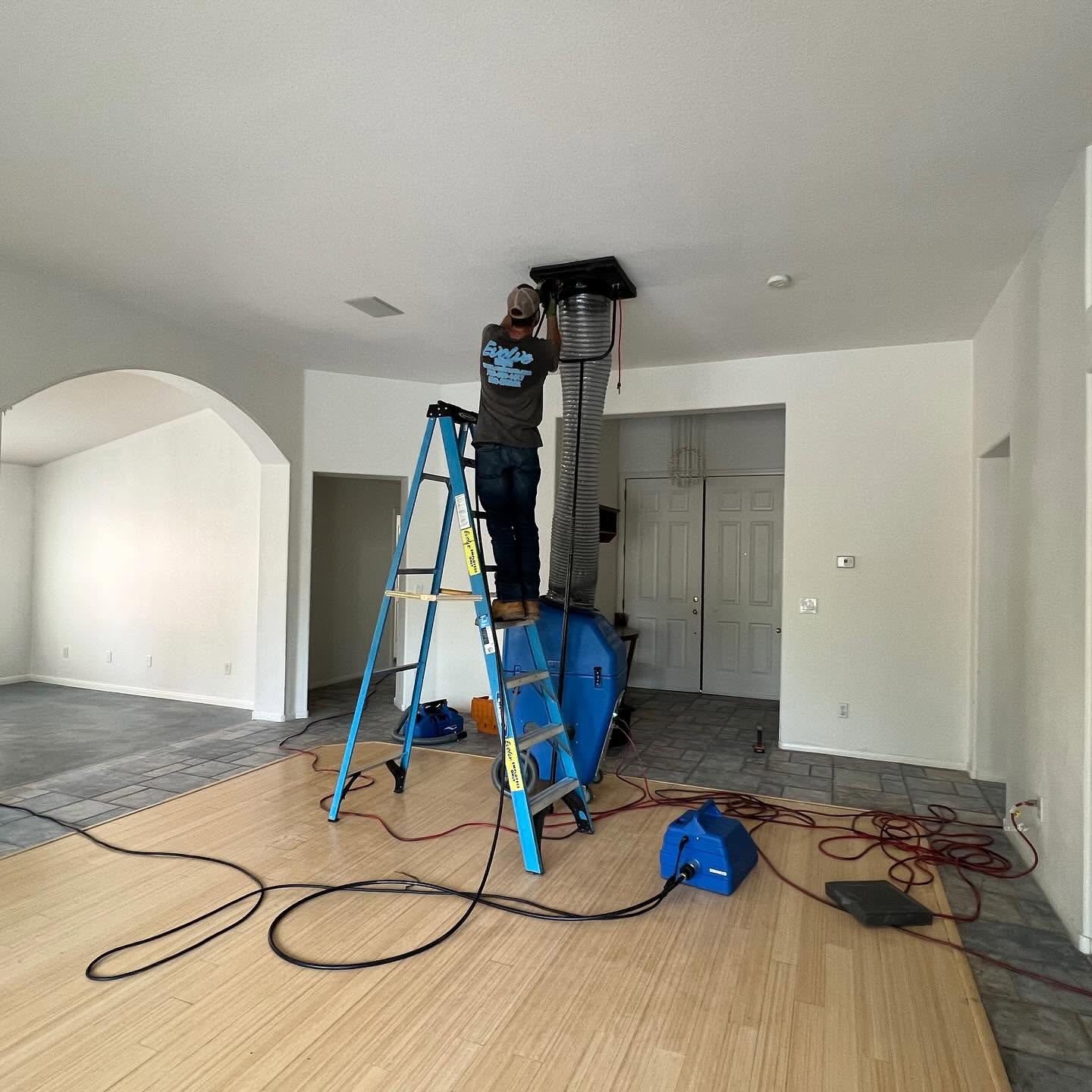 Technician on a ladder cleaning air ducts in a residential home.