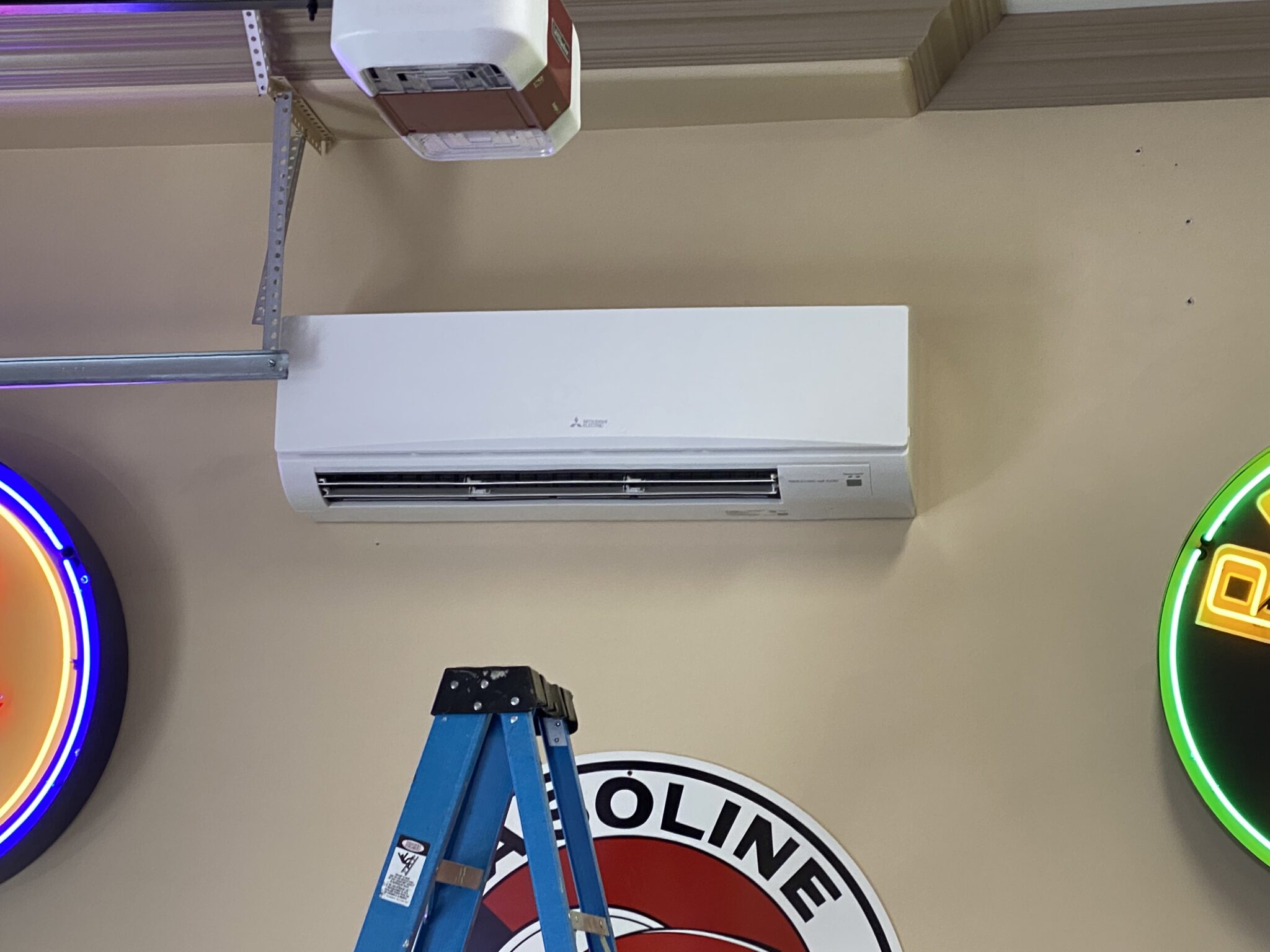 Wall-mounted air conditioning unit installed above a ladder in a room with neon signs.