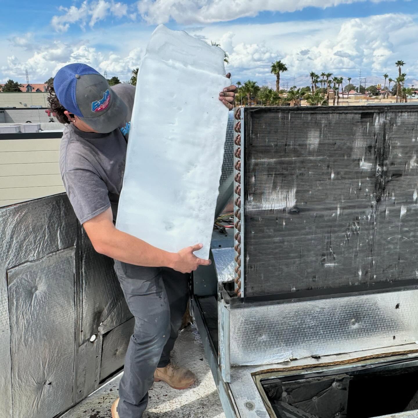 Technician removing a large ice block from an HVAC unit on a rooftop.