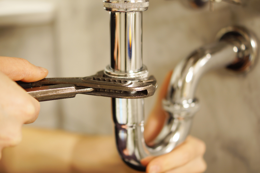 Close-up of hands using a wrench to tighten a pipe under a sink