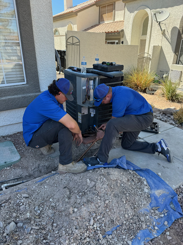 Two HVAC technicians repairing an outdoor air conditioning unit in a residential area.