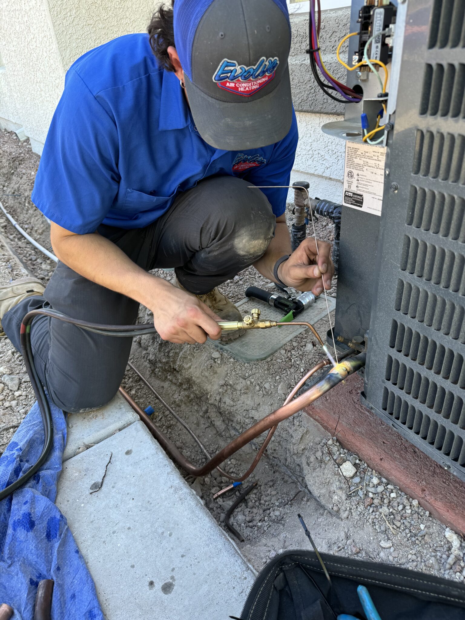Technician in blue uniform repairing an outdoor air conditioning unit.