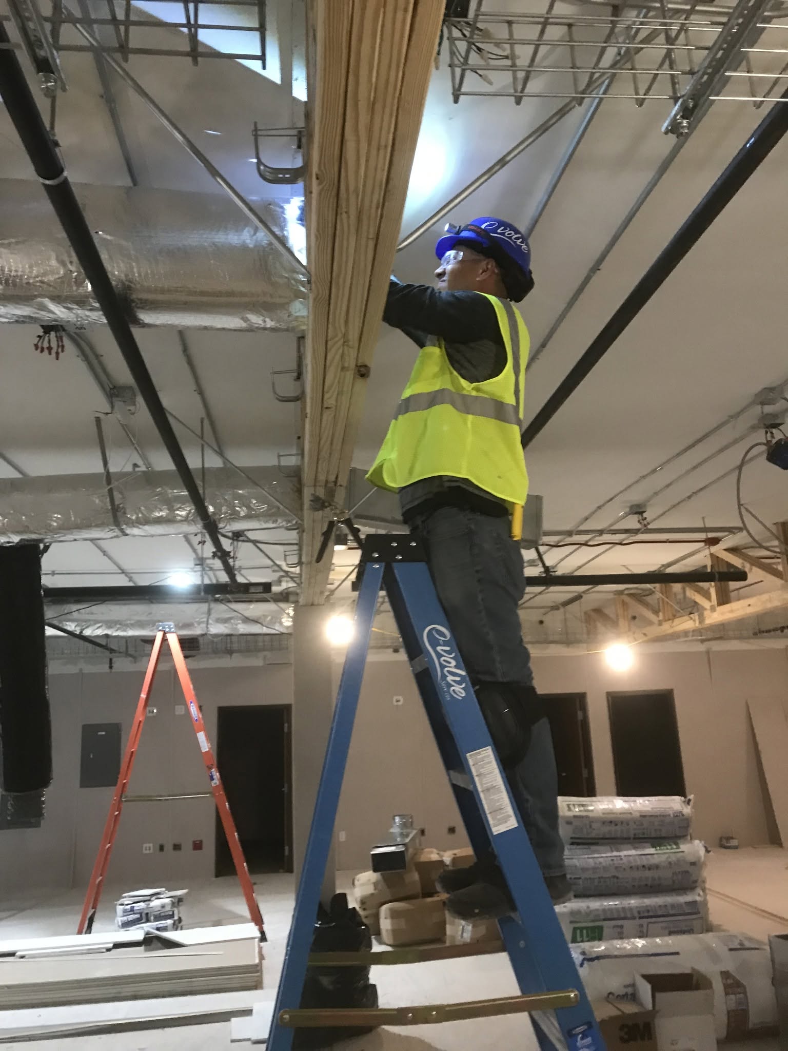 Technician in safety gear working on HVAC installation from a ladder in a commercial building.
