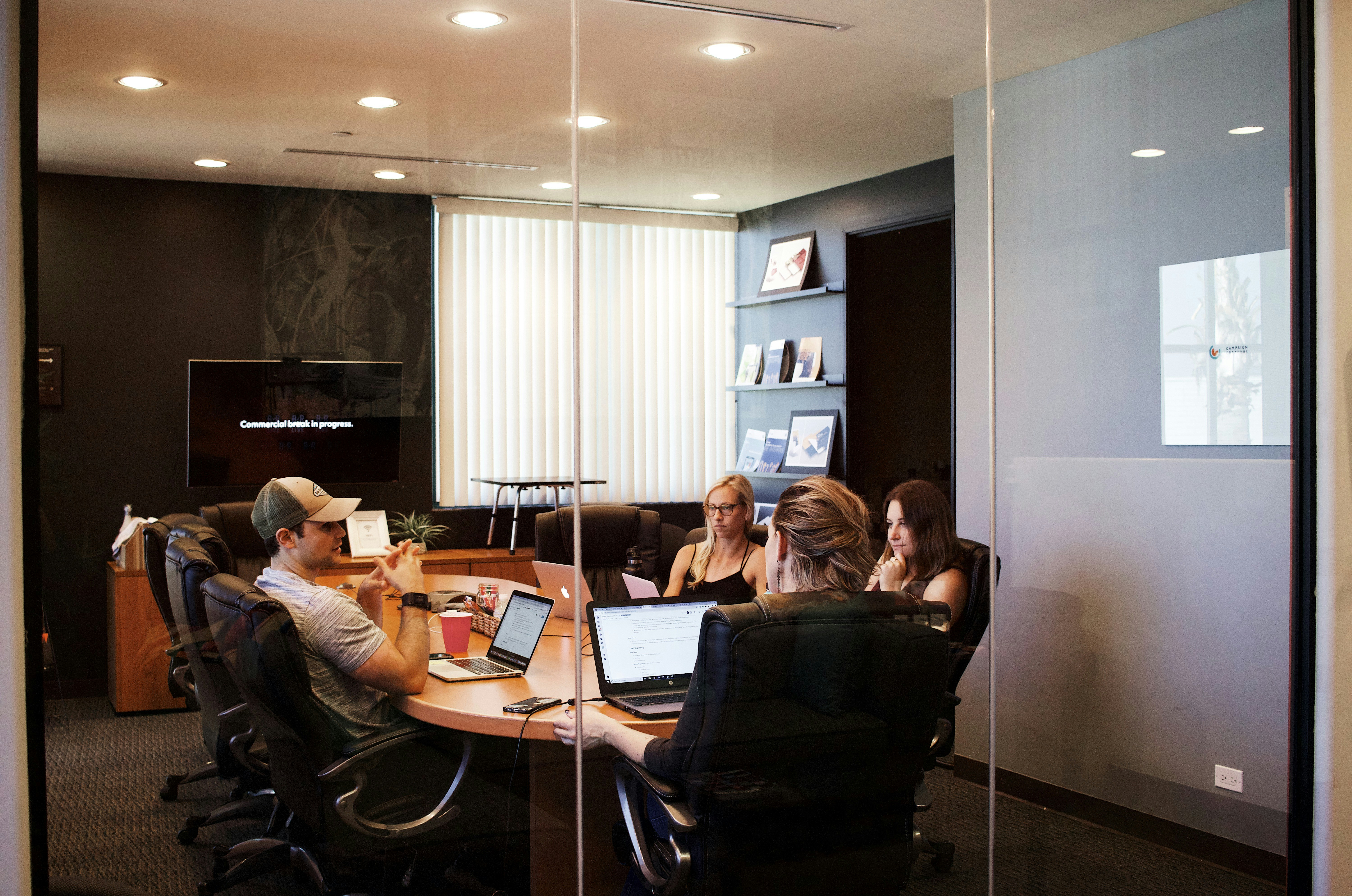 Two people discussing documents at a table with a laptop in a bright office