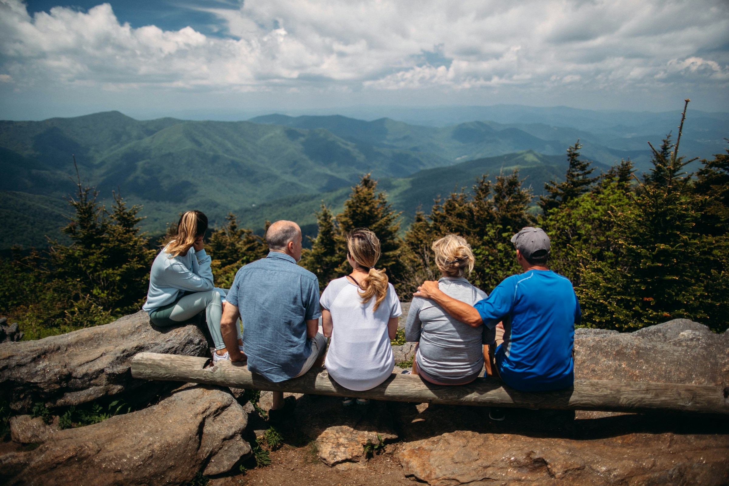 Group of people sitting on a log overlooking a mountain landscape