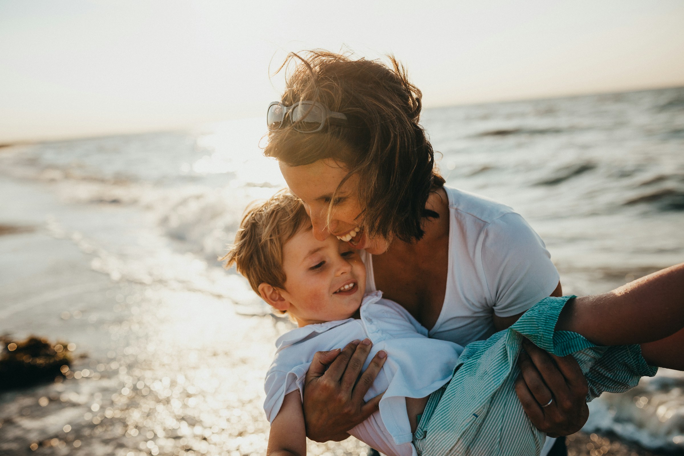 Parent holding child while smiling on a beach at sunset
