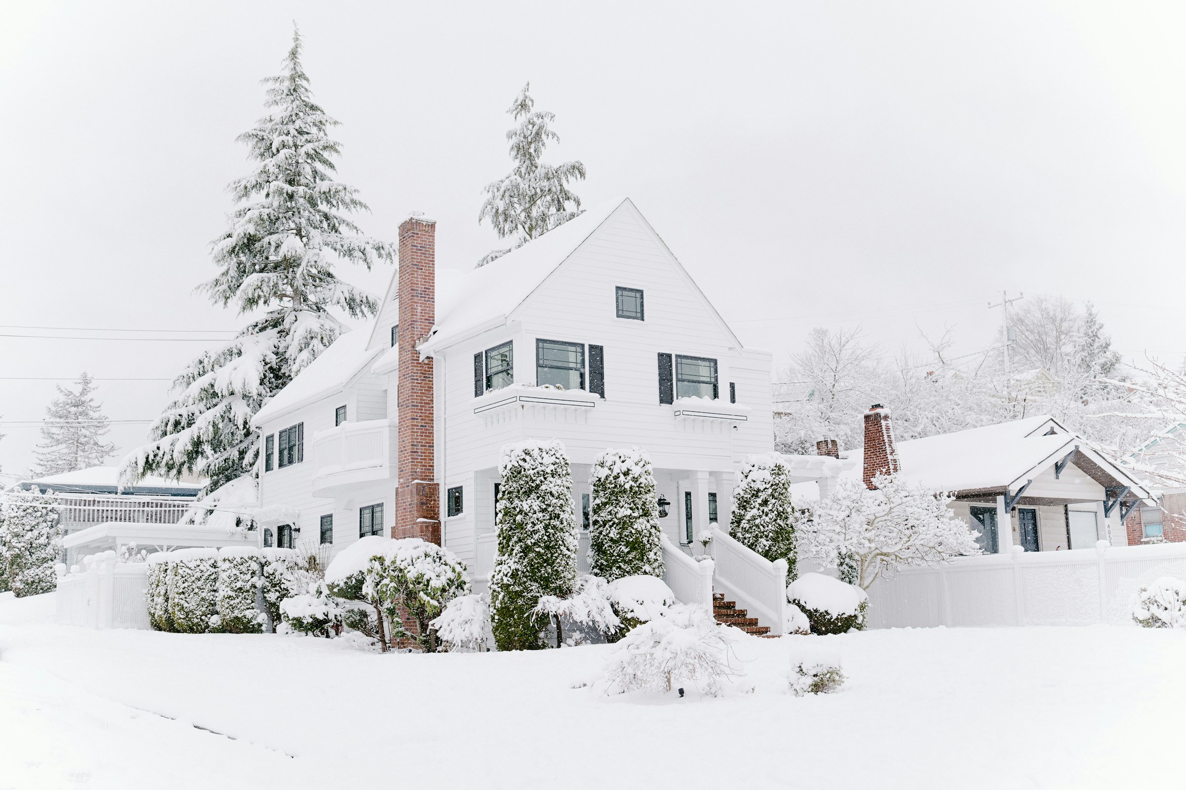 Snow-covered suburban house with trees and a chimney