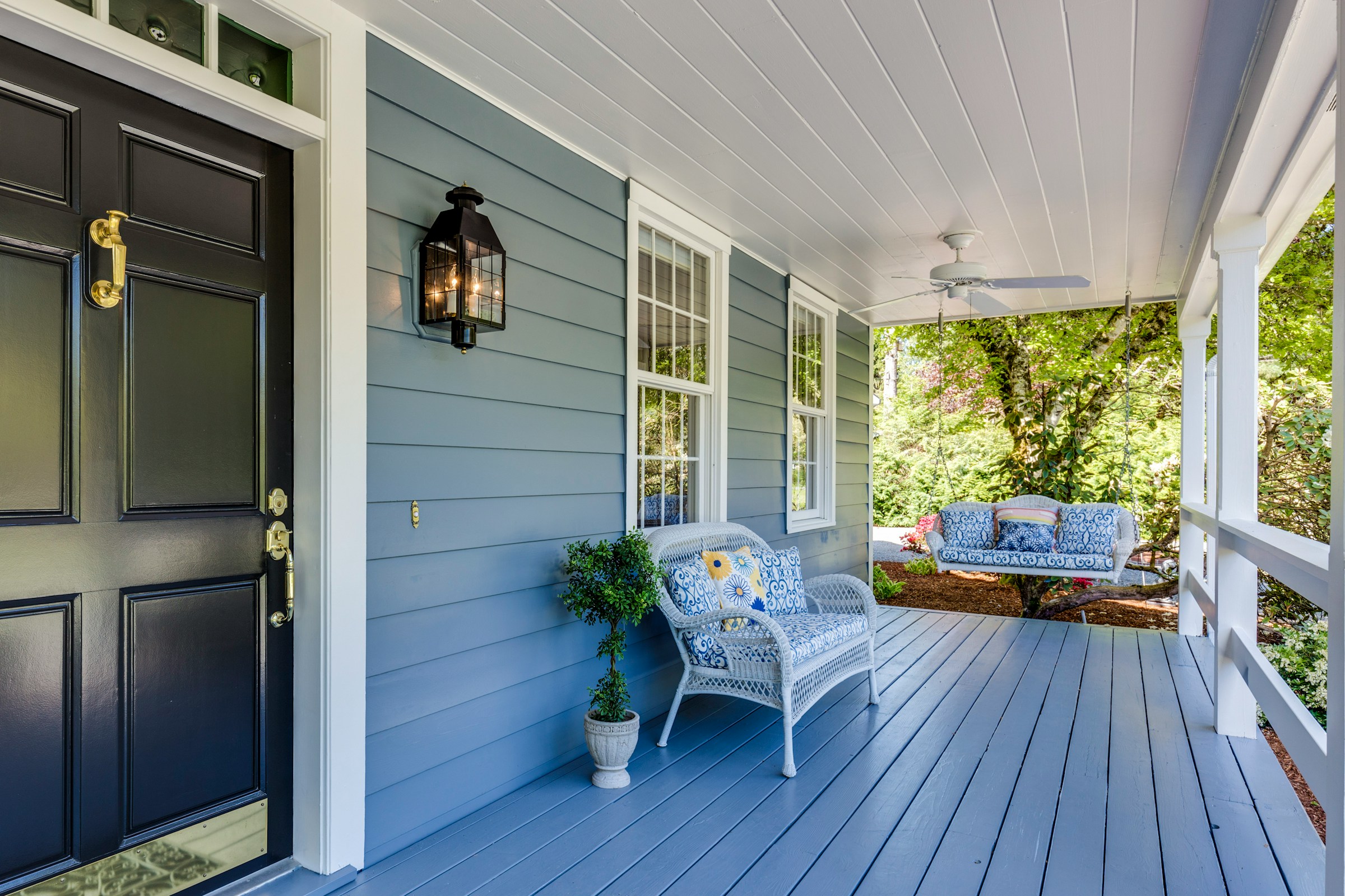 Front porch with blue siding, wicker chair, and hanging light fixture