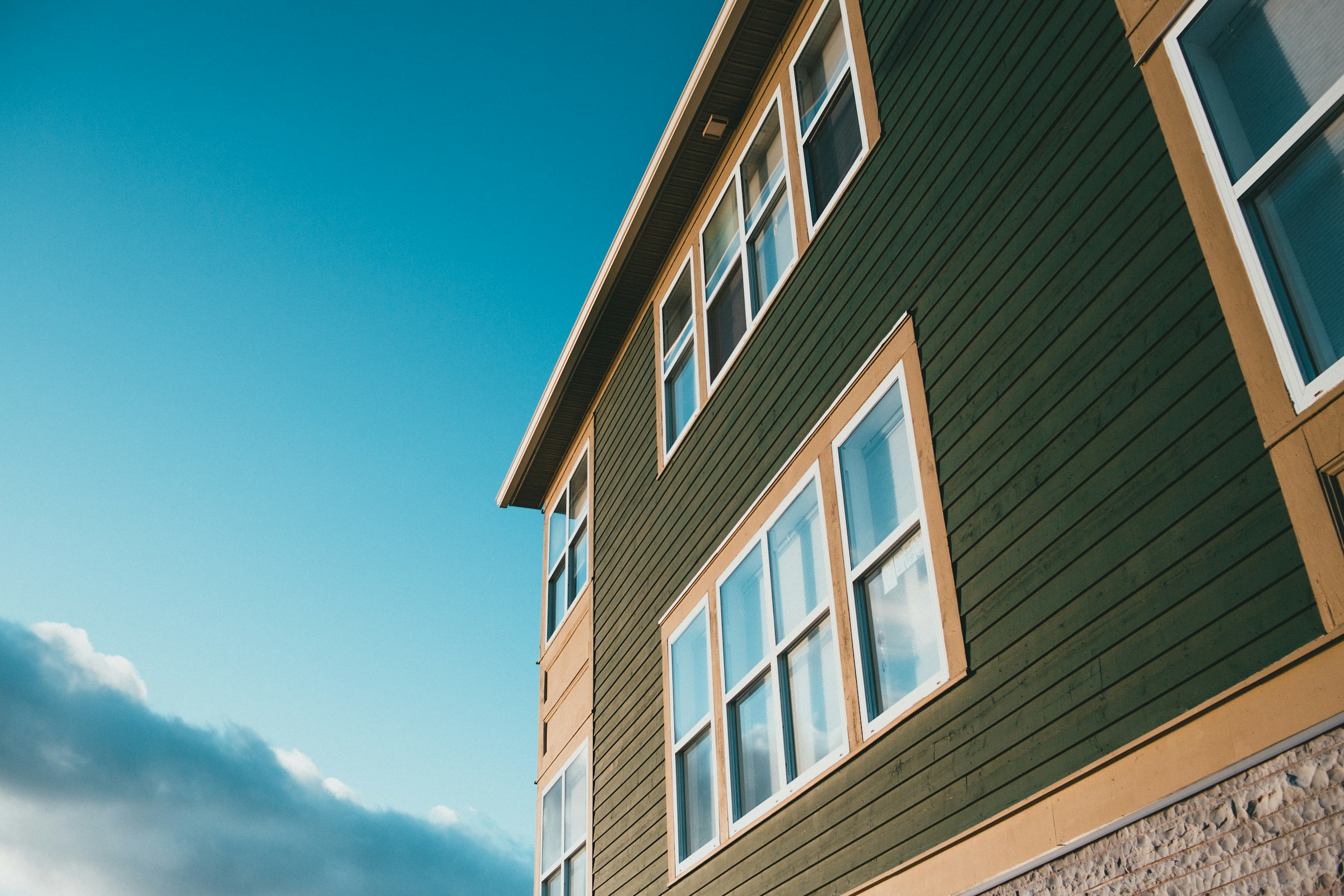 Low angle view of a green building with multiple windows against a blue sky