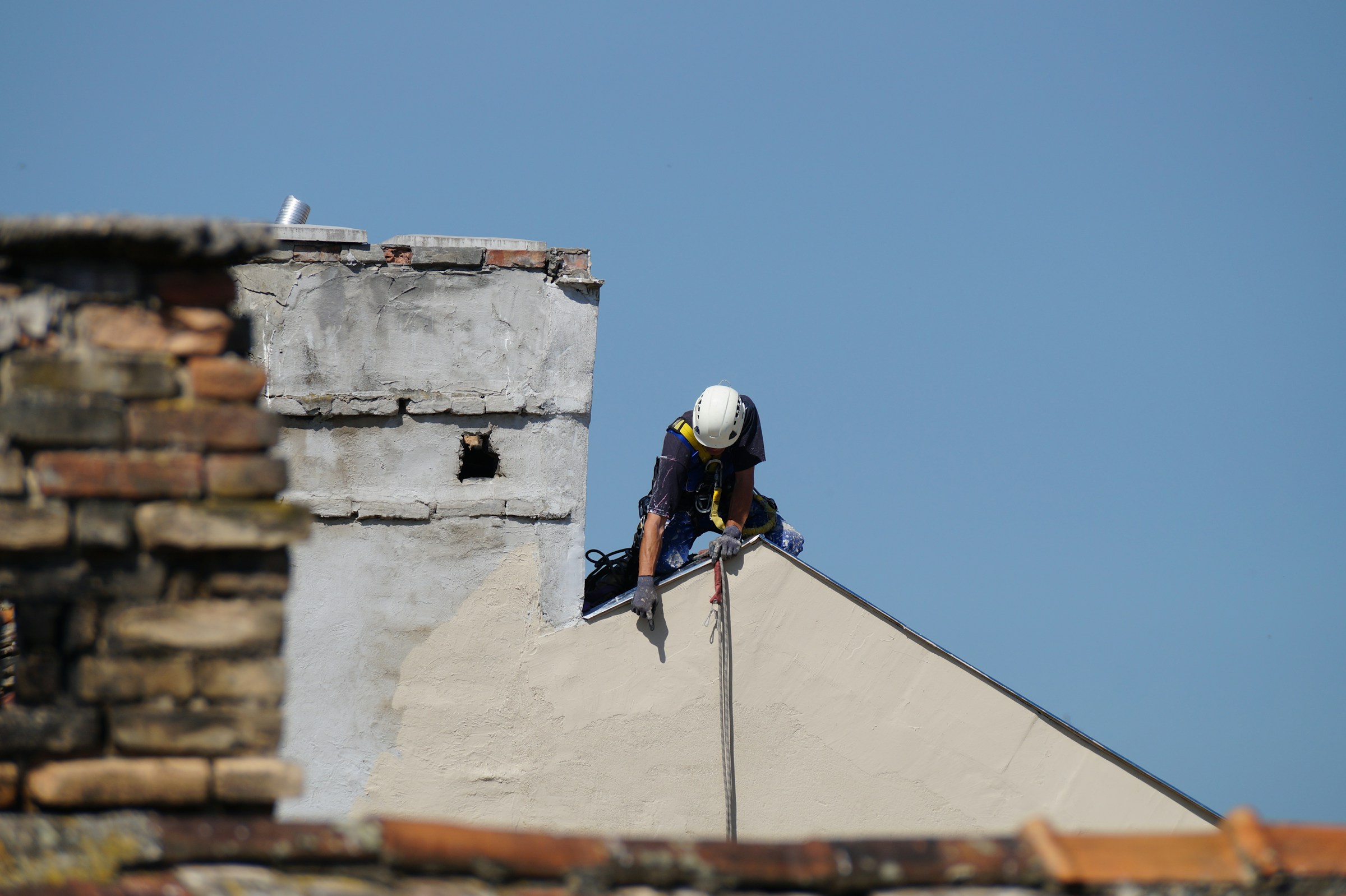 Worker in safety gear repairing a rooftop under a clear blue sky