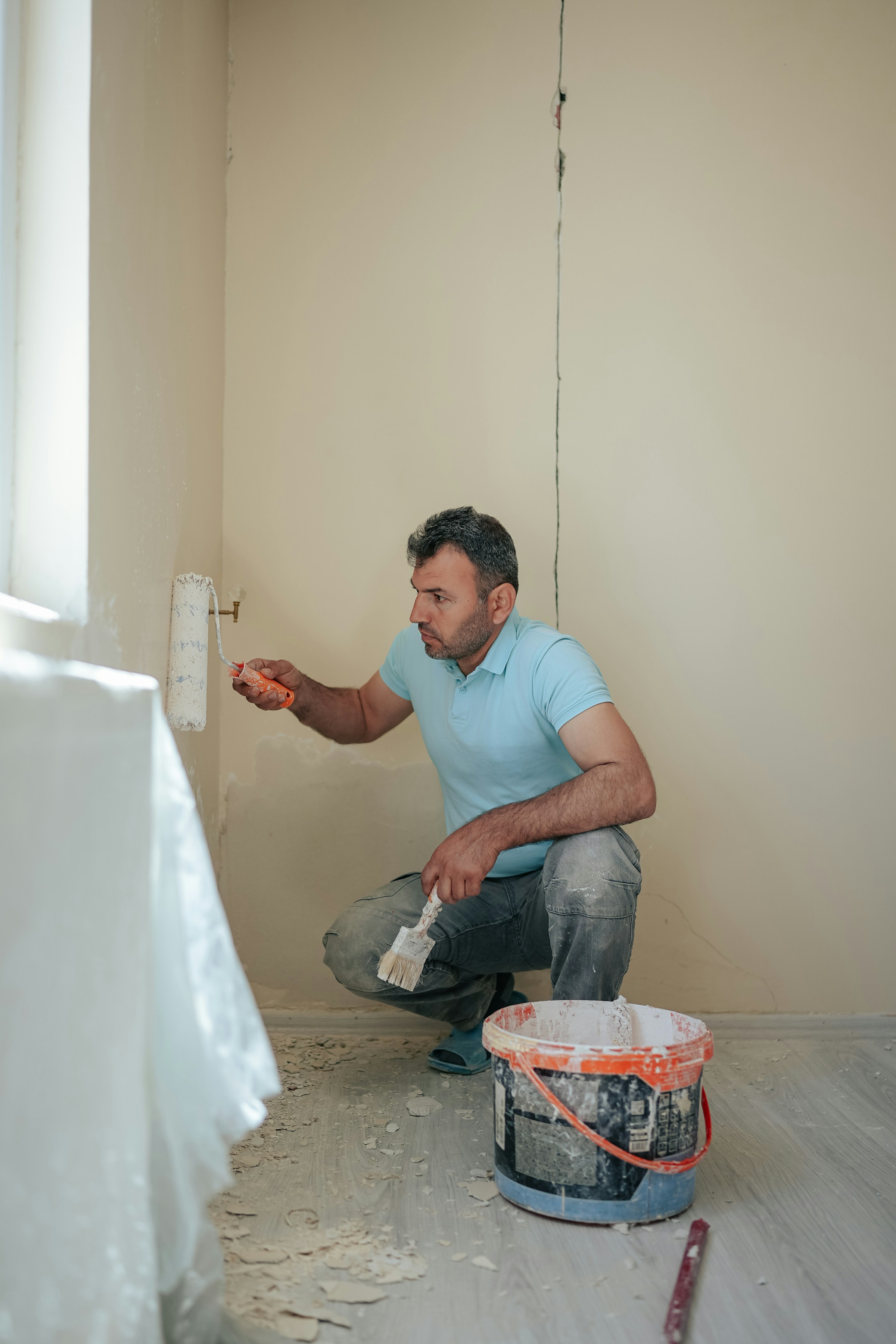 Man painting a wall with a roller in a room with a crack in the wall