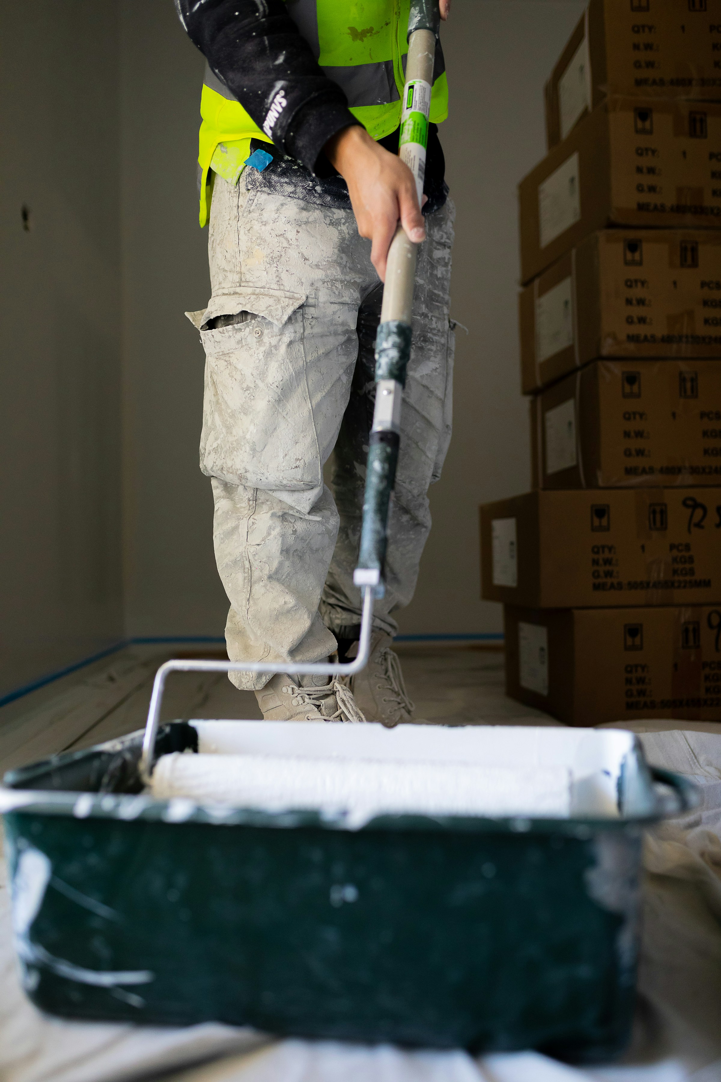 Person in work clothes using a paint roller with white paint