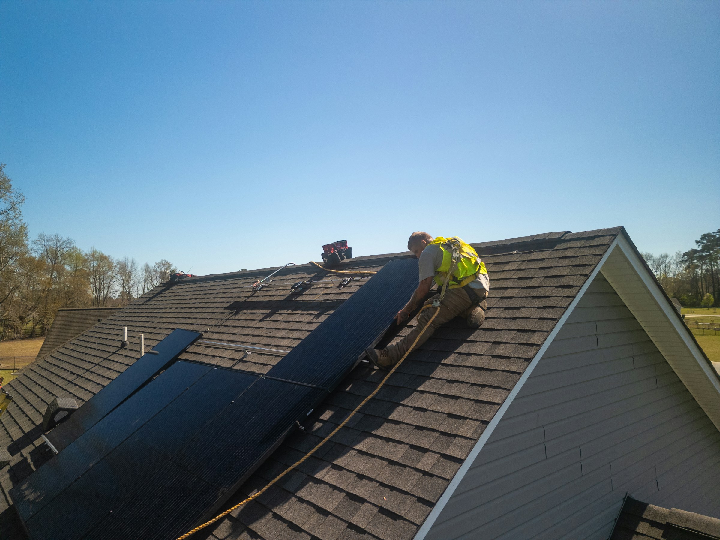 Worker installing solar panels on a residential roof under a clear blue sky
