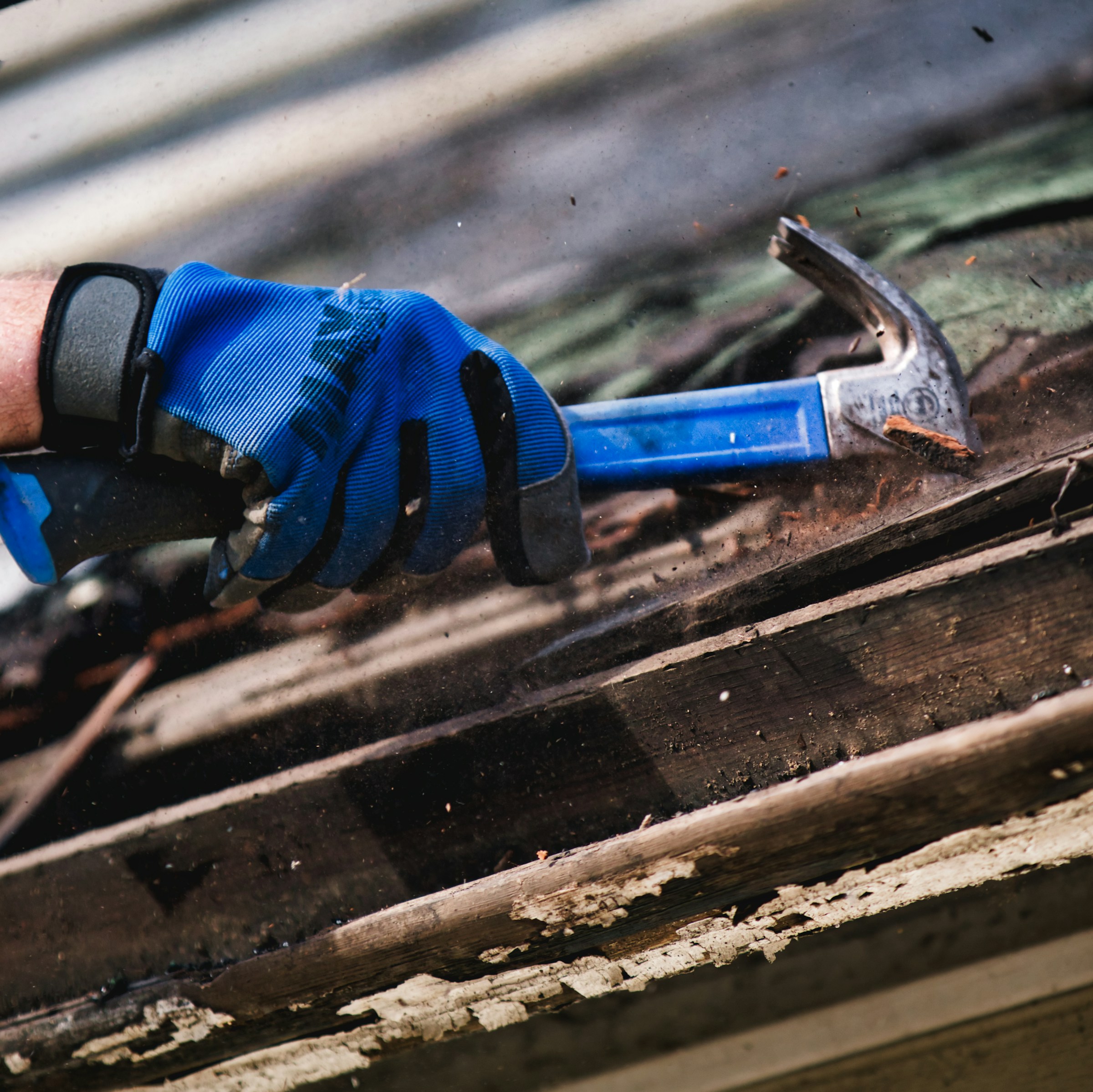 Close-up of a person using a hammer to remove old roofing materials.