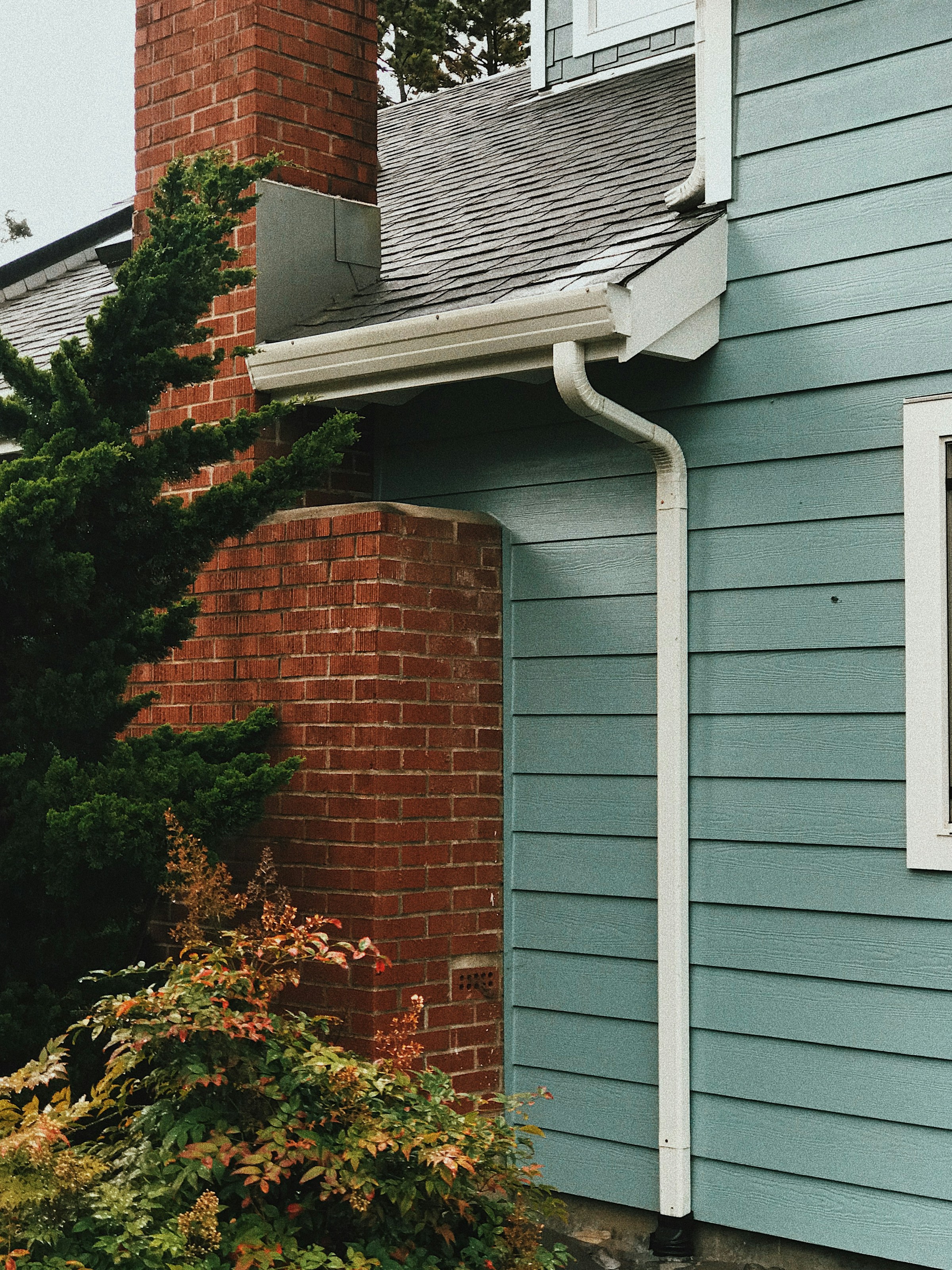 Close-up of a house exterior with blue siding, brick chimney, and white gutter.