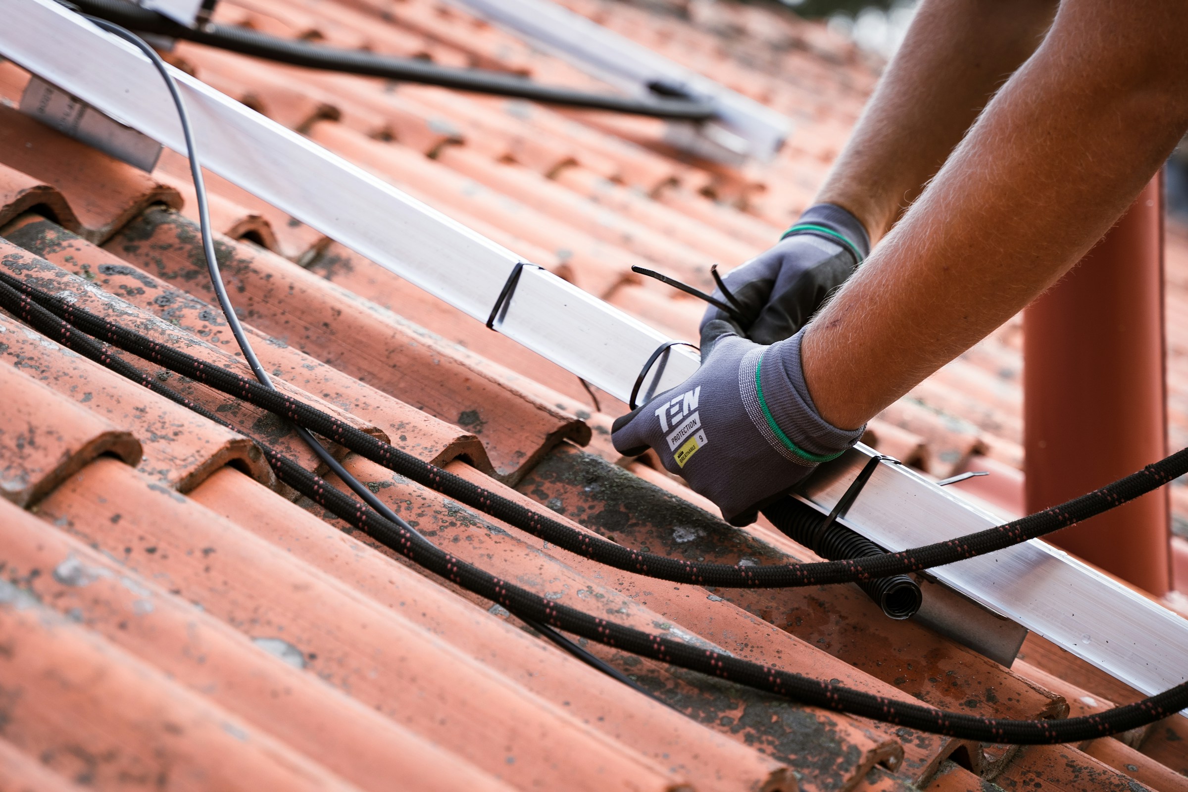 Person securing cables on a tiled roof with a ladder