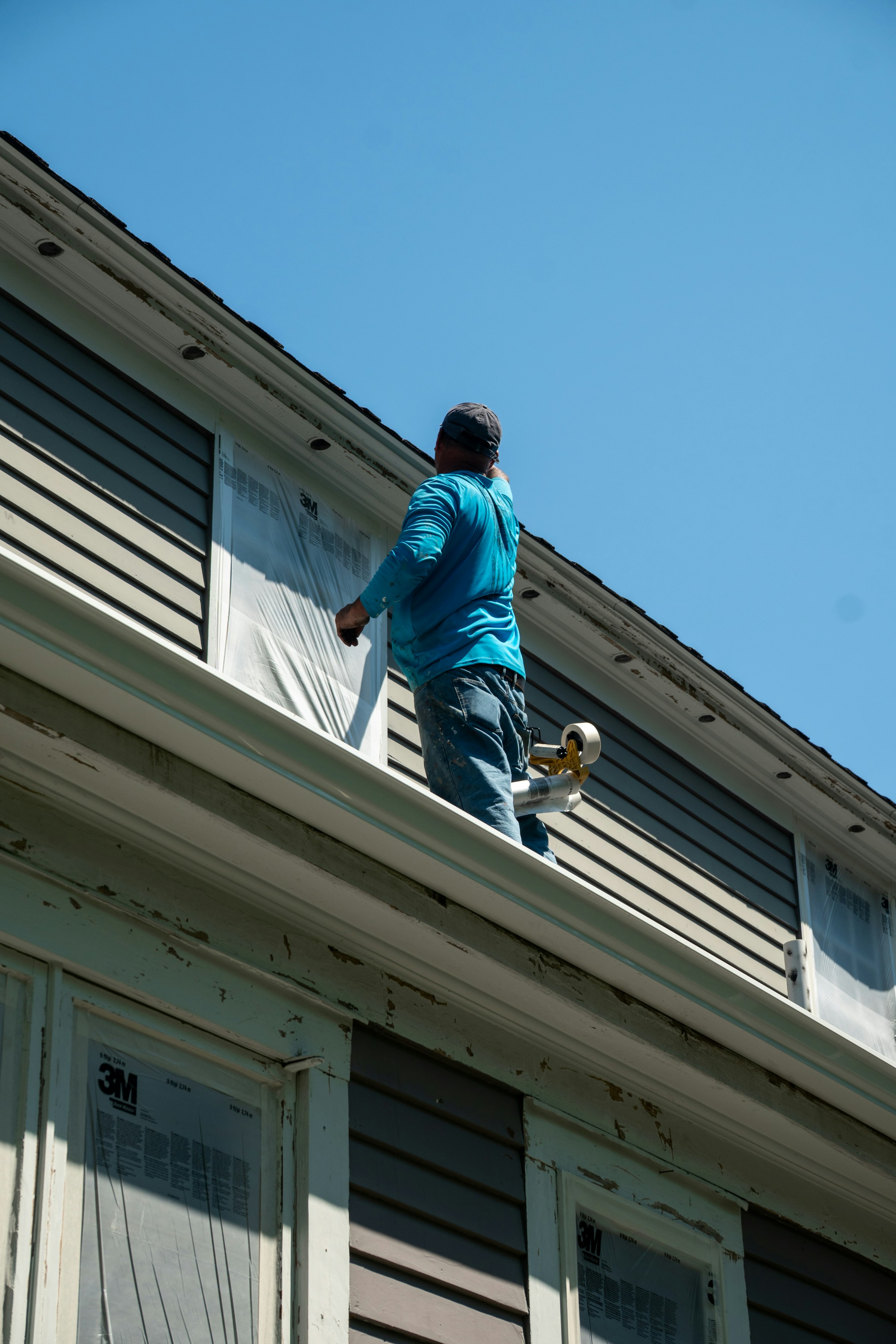 Worker painting the exterior of a house with protective coverings on windows