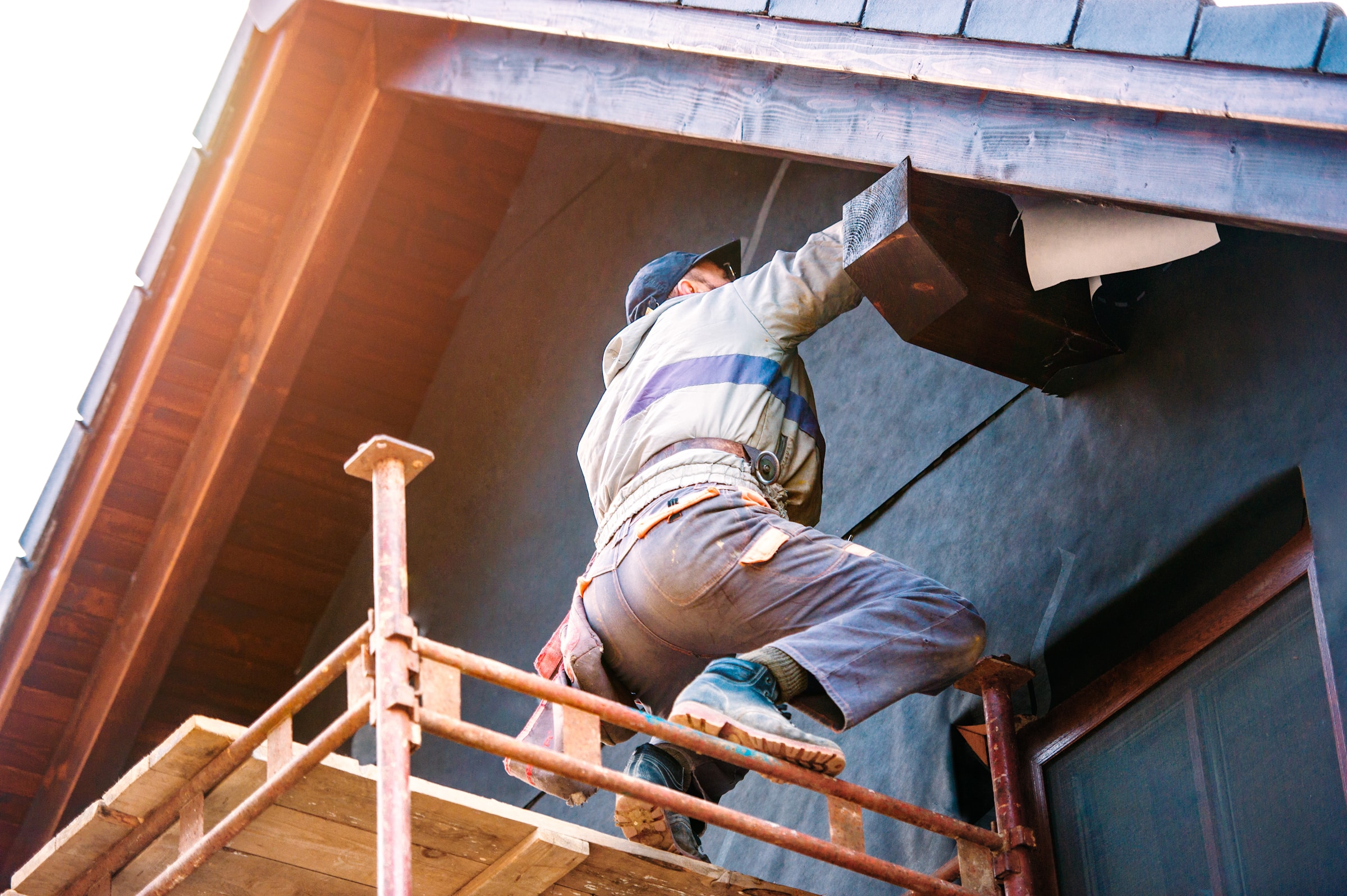 Worker on scaffolding installing roof soffit on a house exterior
