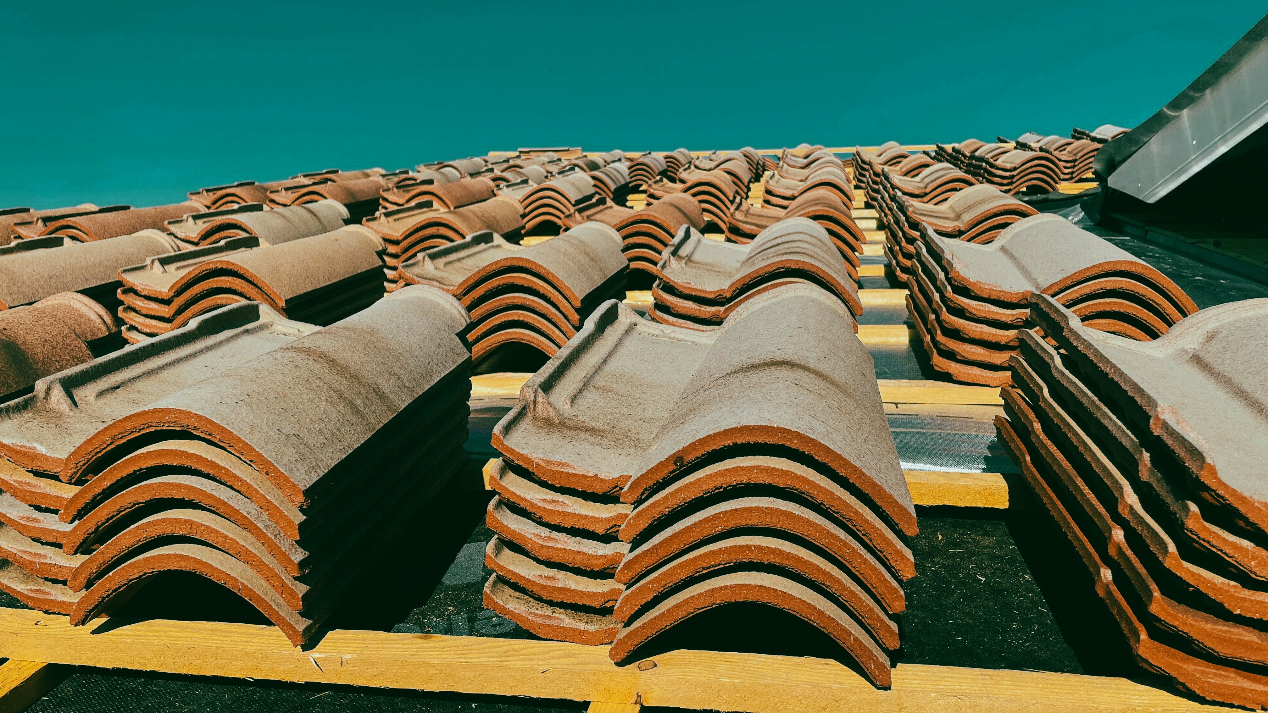 Stacks of red clay roofing tiles on a rooftop under a clear sky