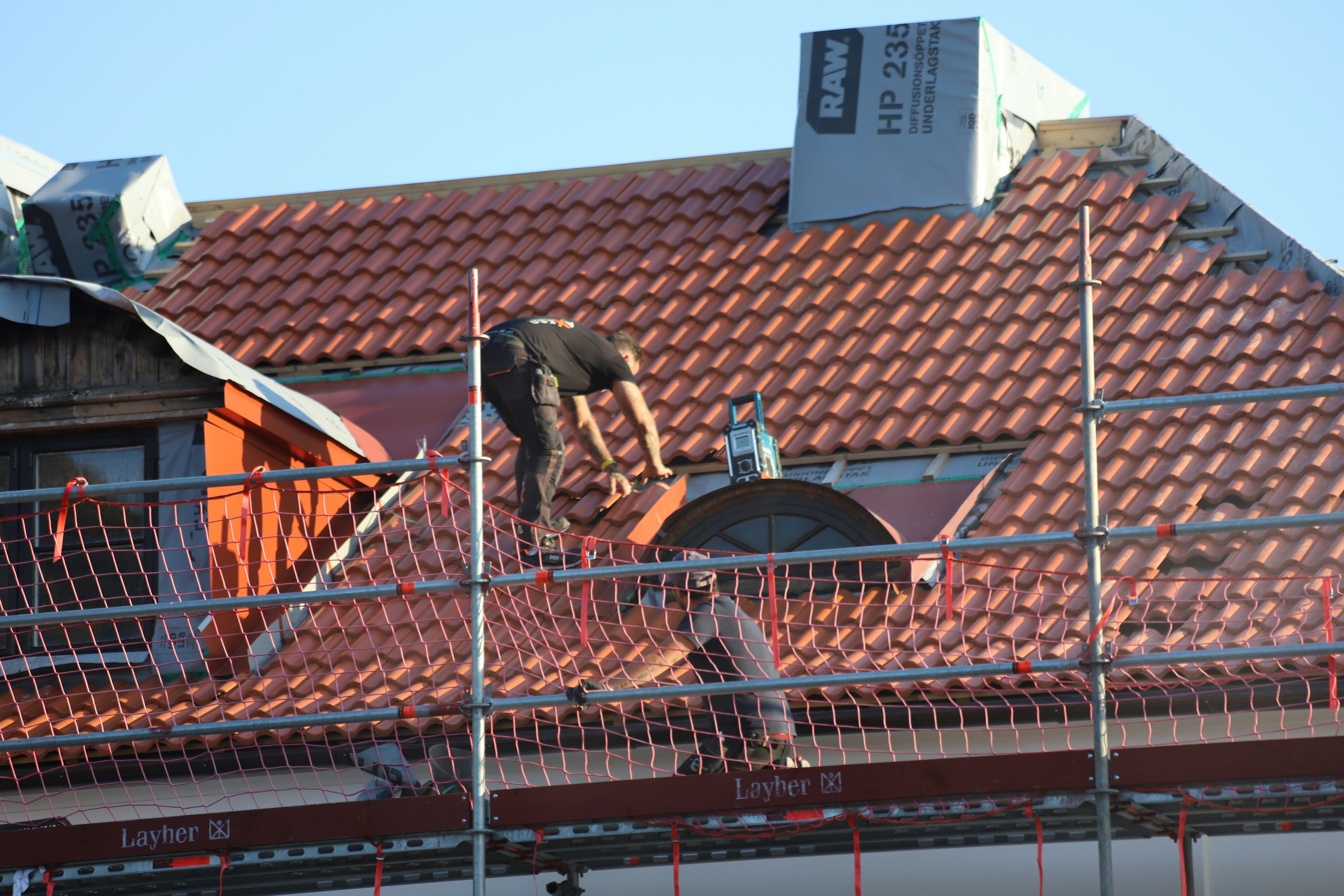 Worker installing red roof tiles on a house under construction