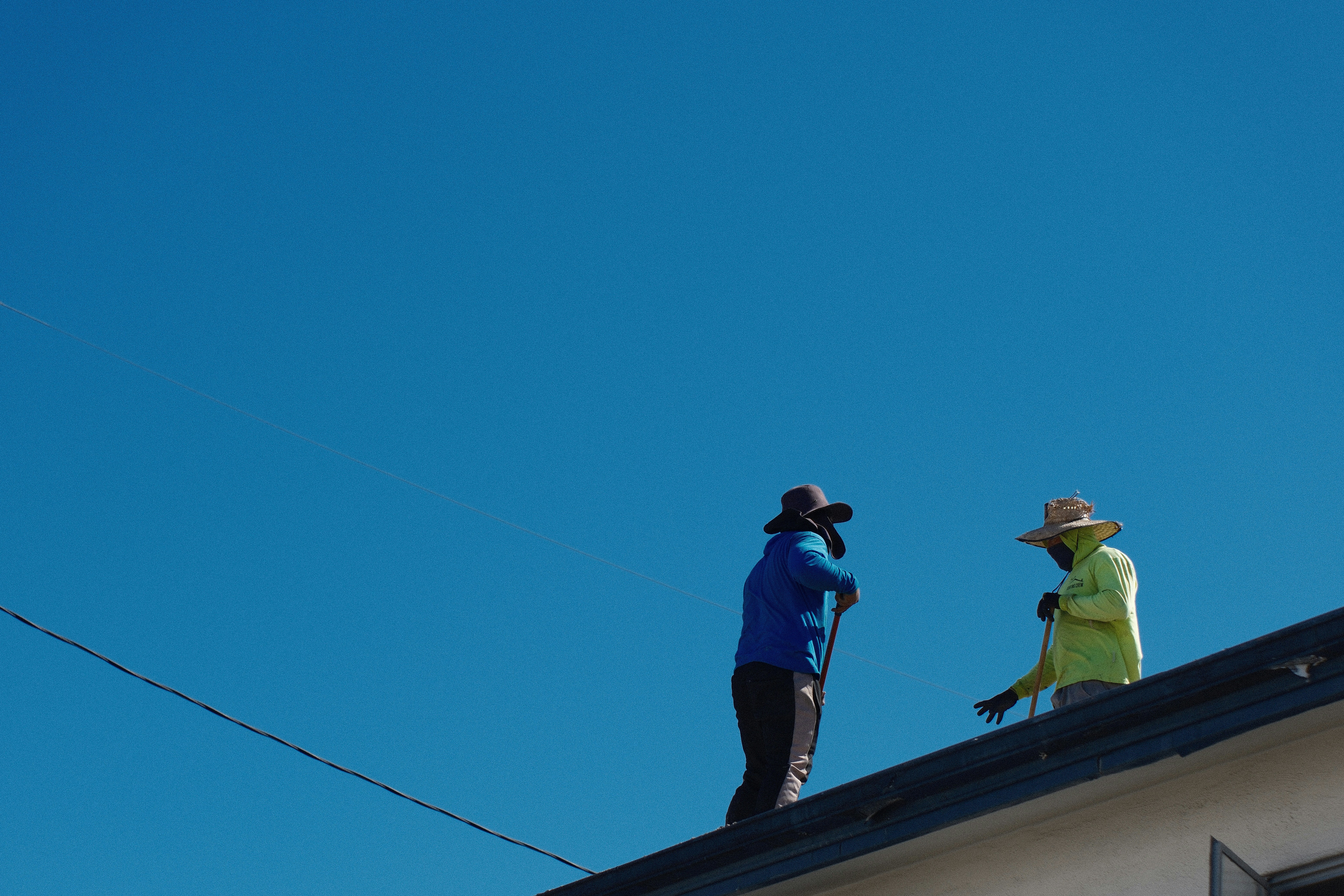 Two workers in hats standing on a roof under a clear blue sky