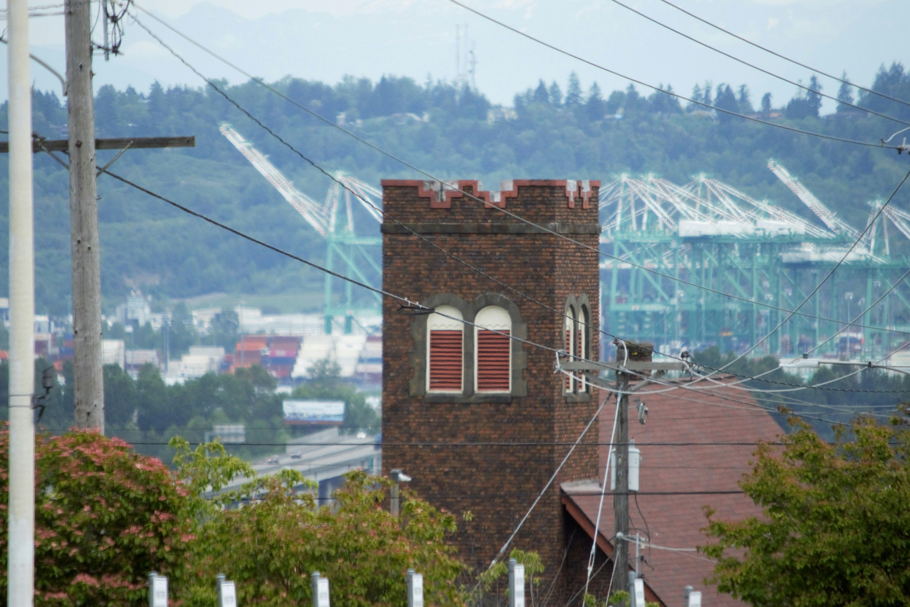 Brick building with a tower and industrial cranes in the background