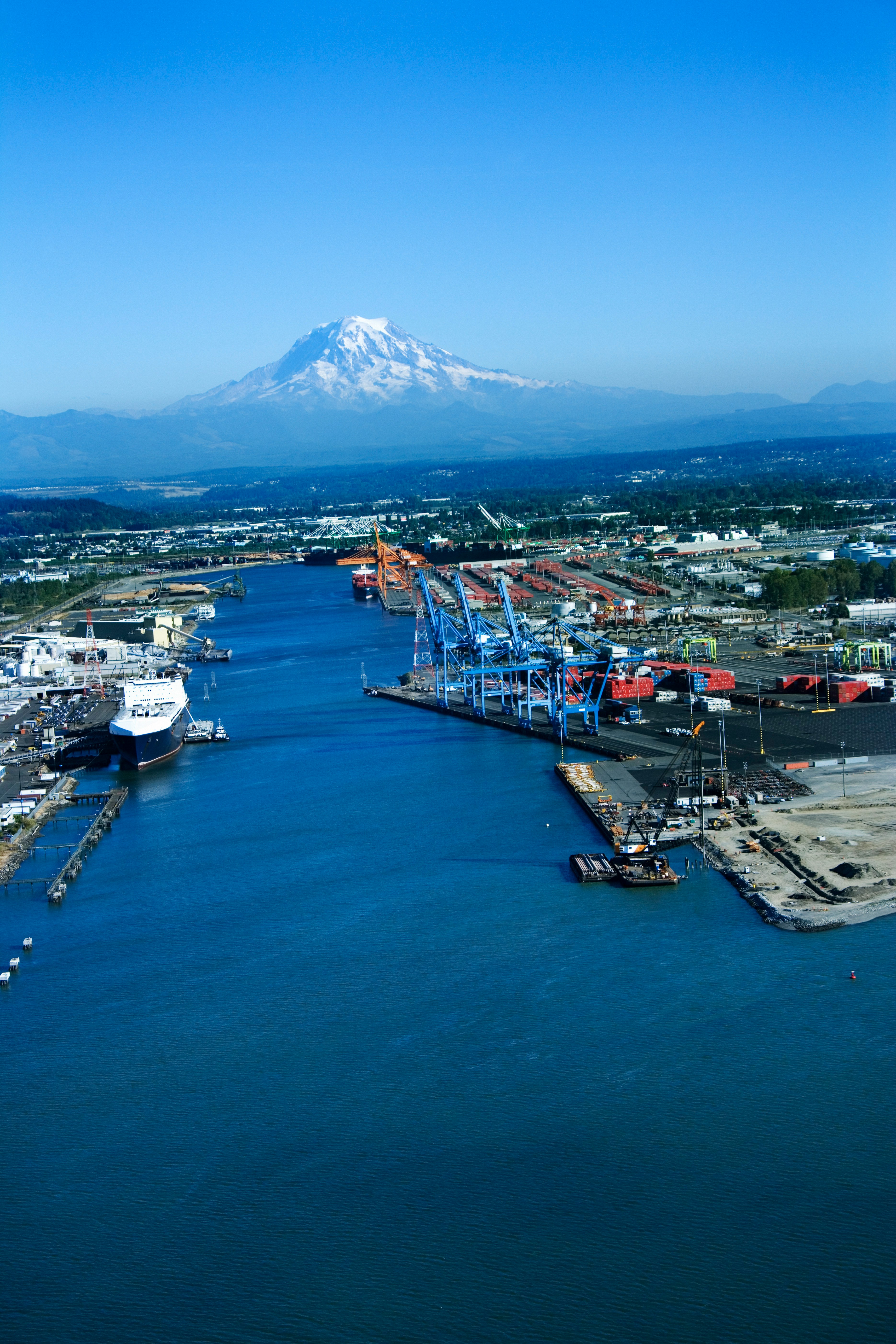 Aerial view of a port with cranes and ships, with a mountain in the background