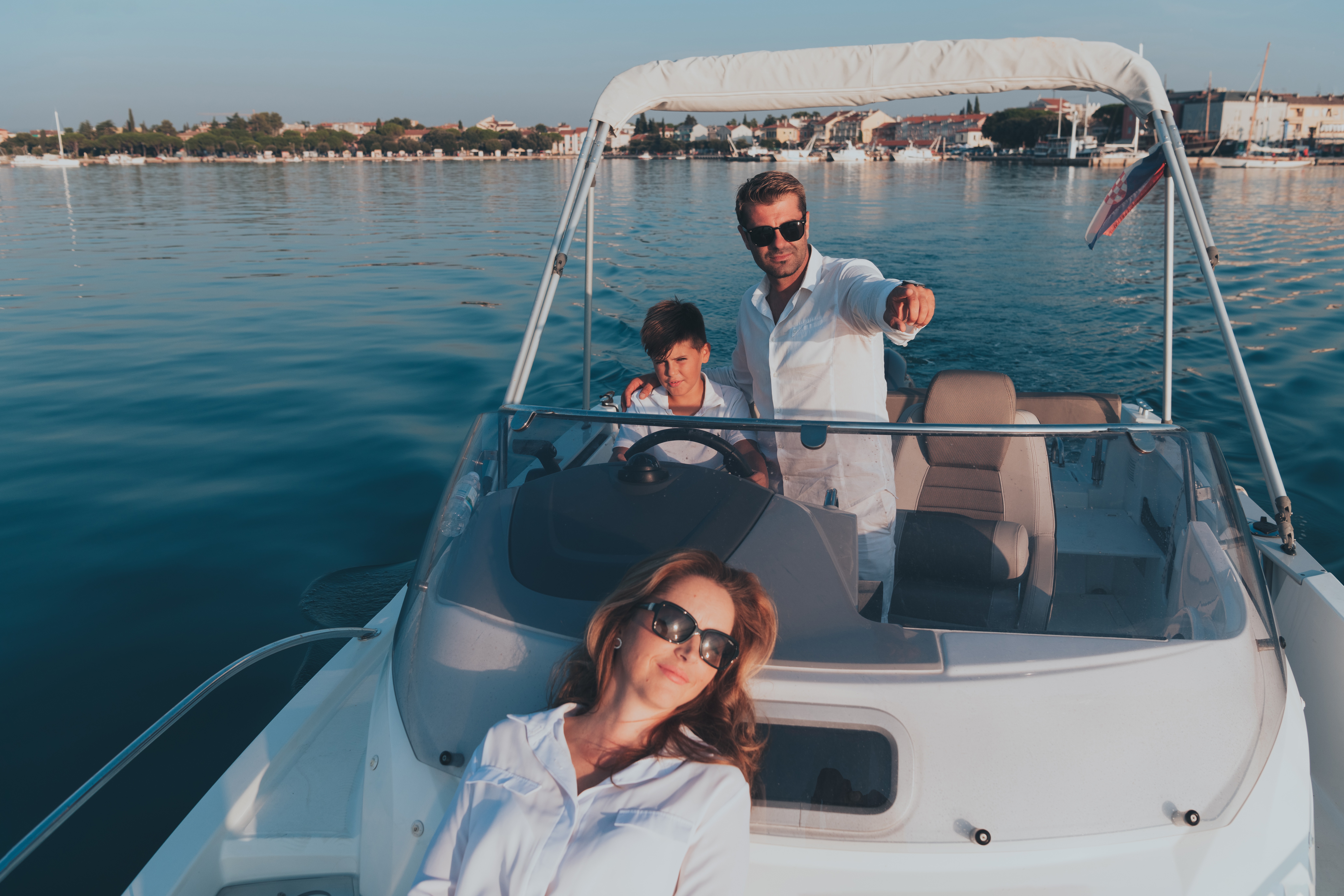 Family enjoying a boat ride on a sunny day with a scenic waterfront view.