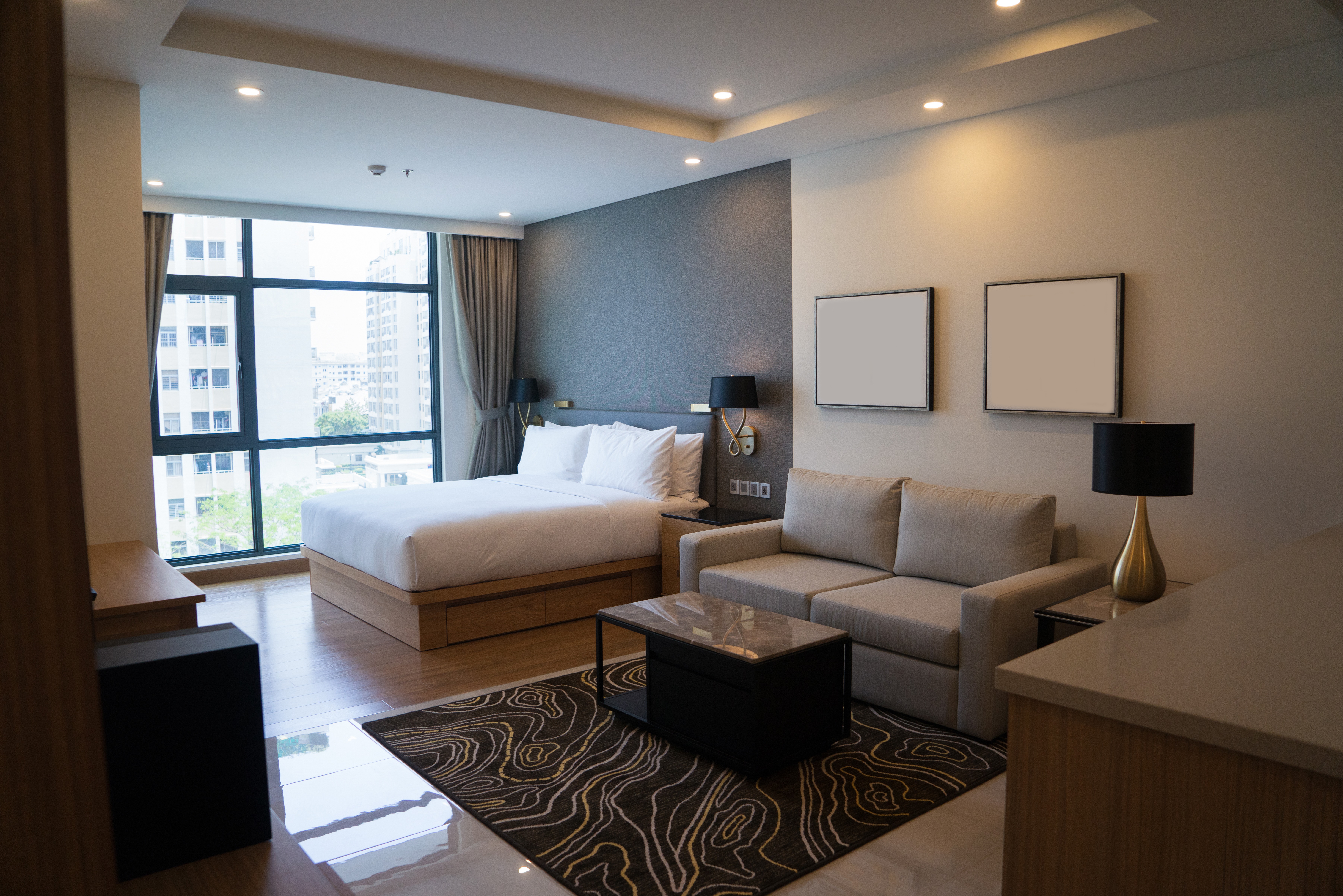 Modern hotel room with a large bed, sofa, and city view window.