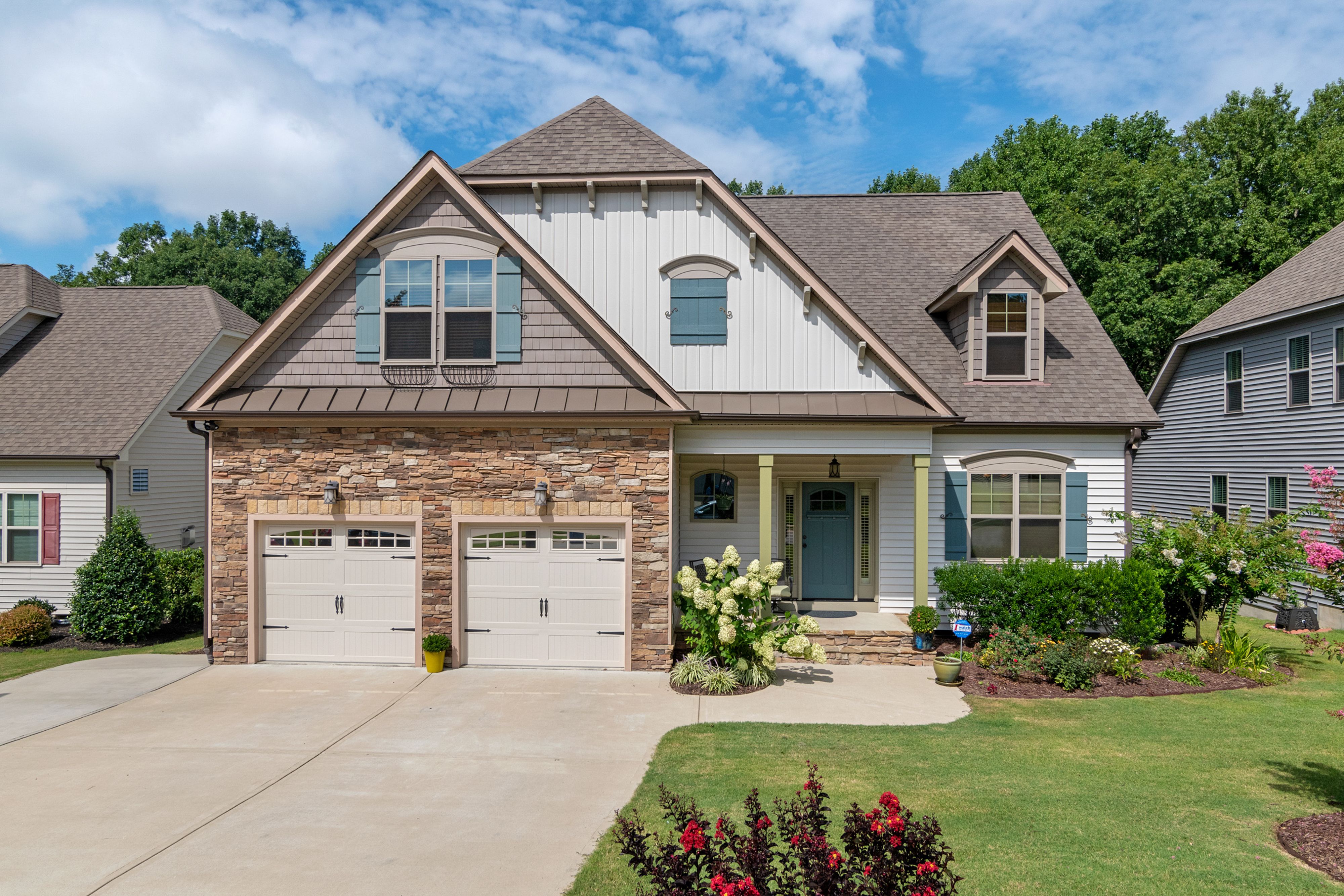 Suburban house with stone and siding exterior, two-car garage, and landscaped yard