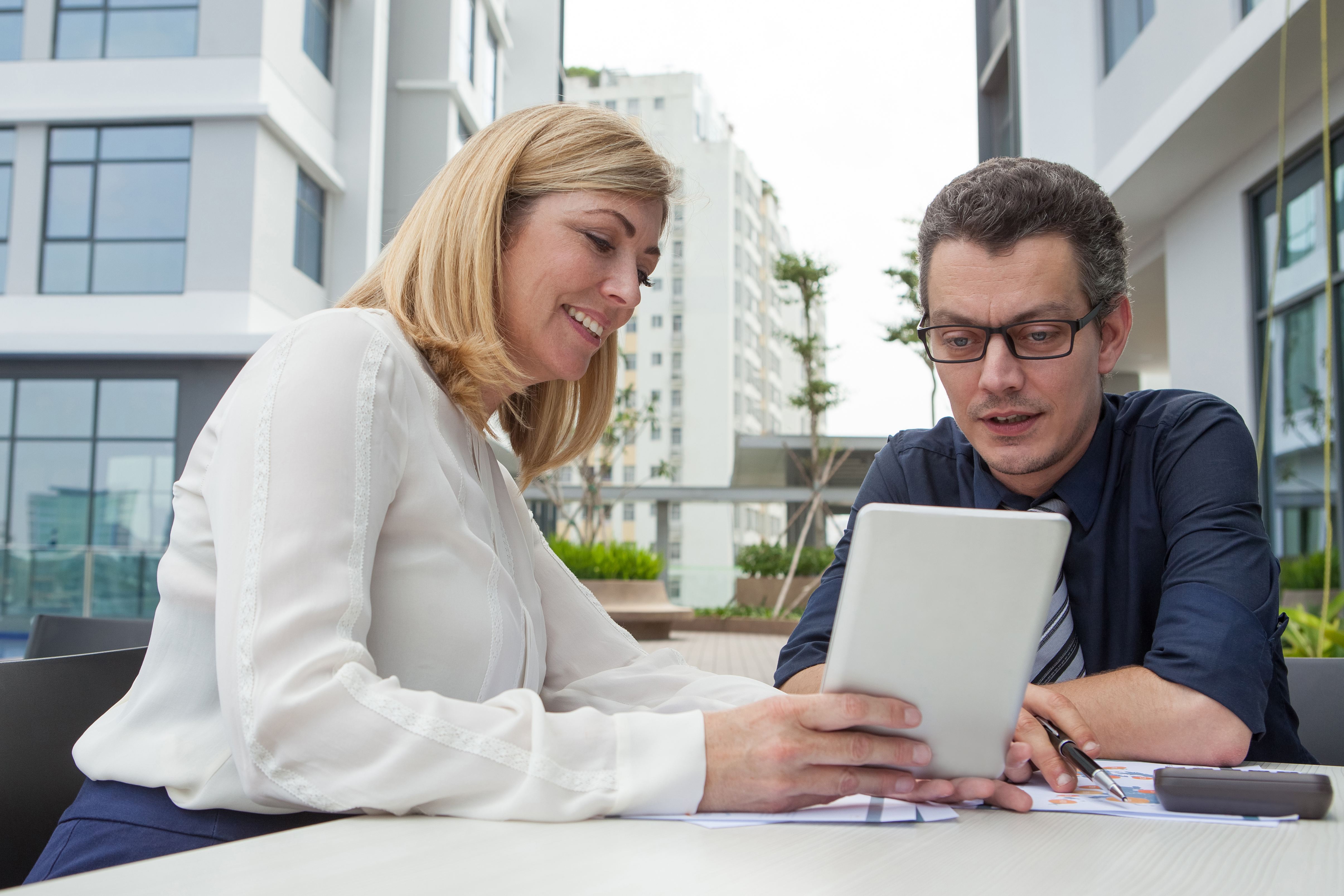Two business professionals discussing over a tablet in an outdoor office setting.