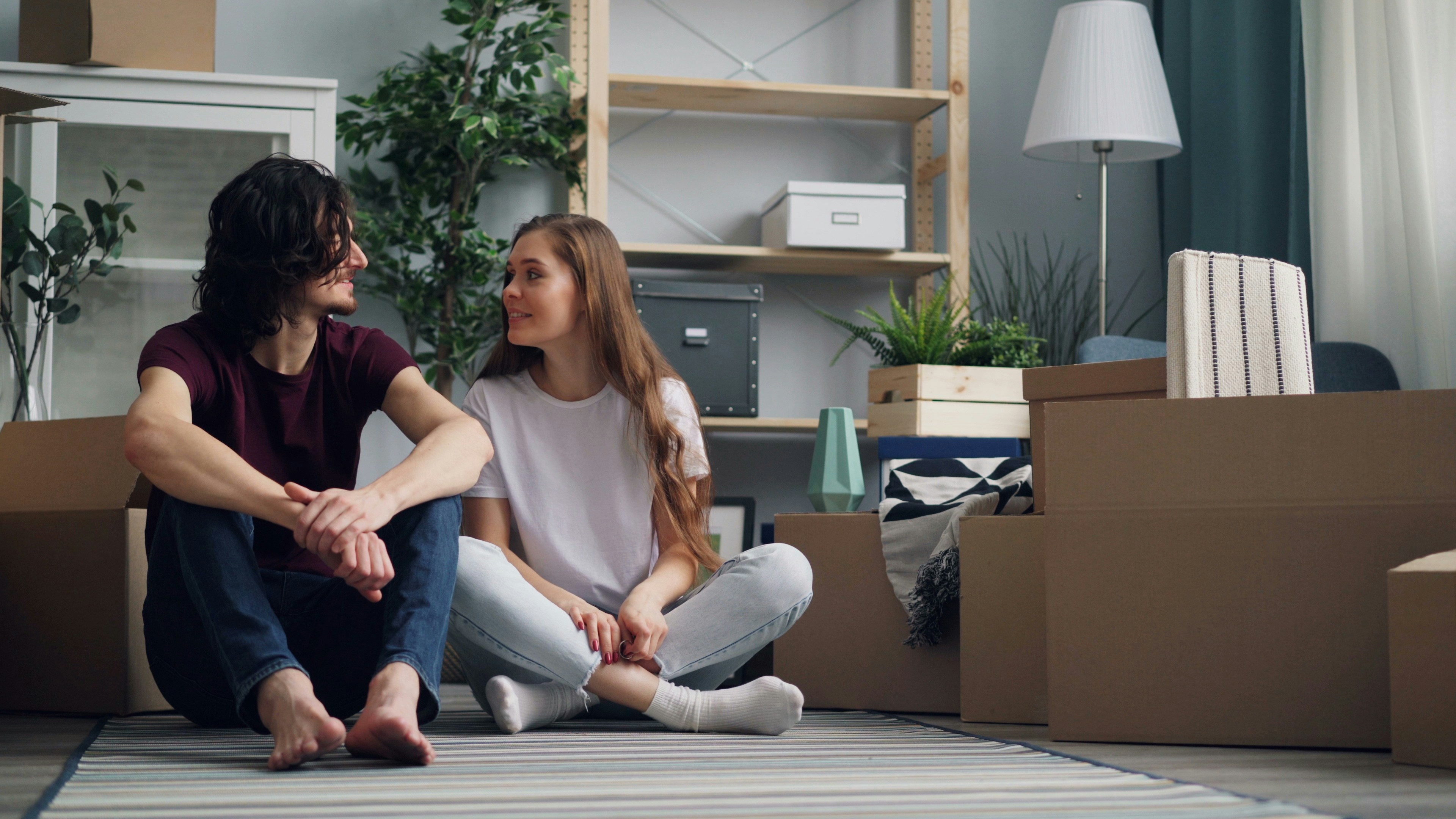 Couple sitting on the floor surrounded by moving boxes in a living room.