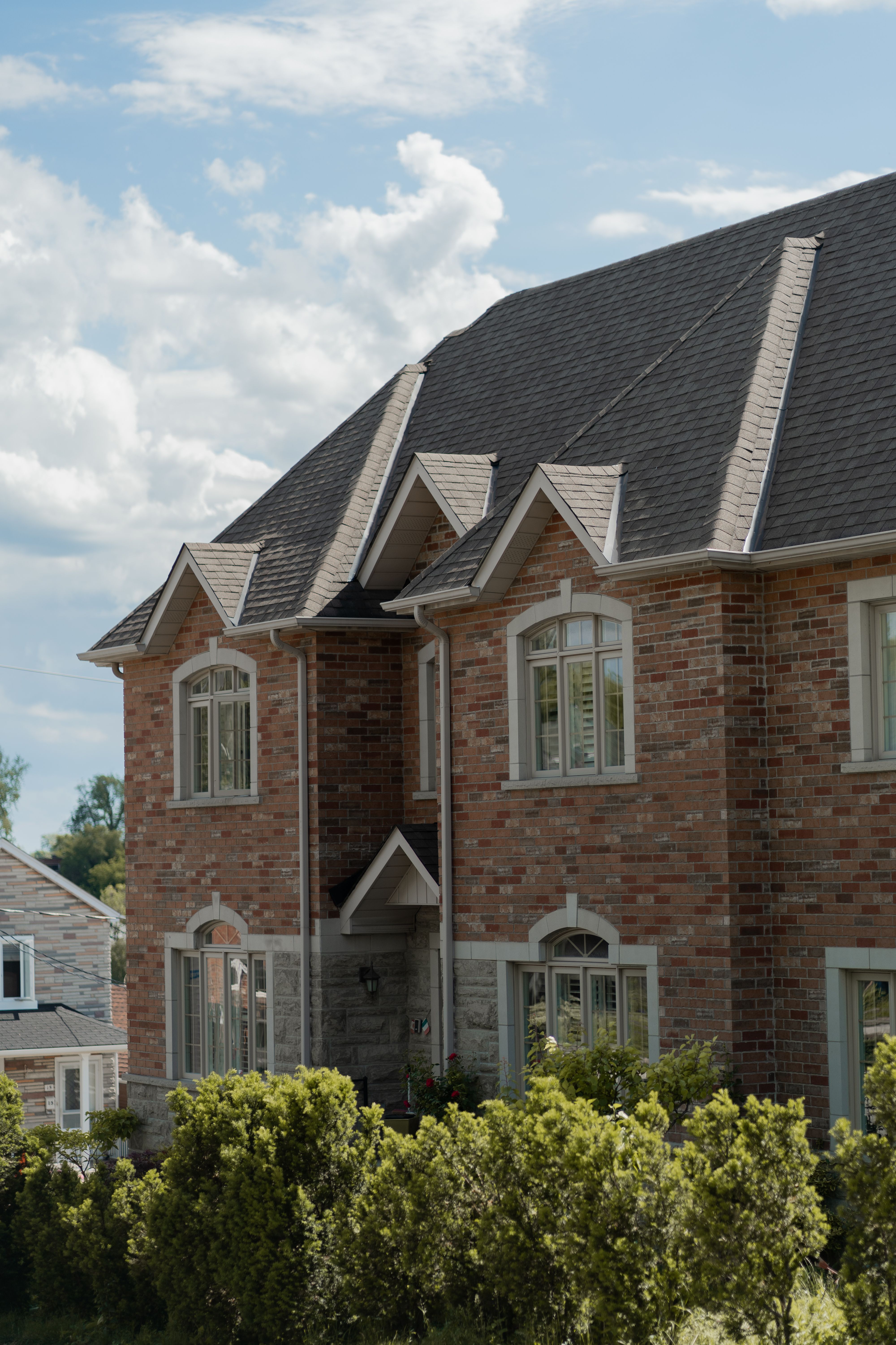 Large brick house with gabled roof and manicured bushes