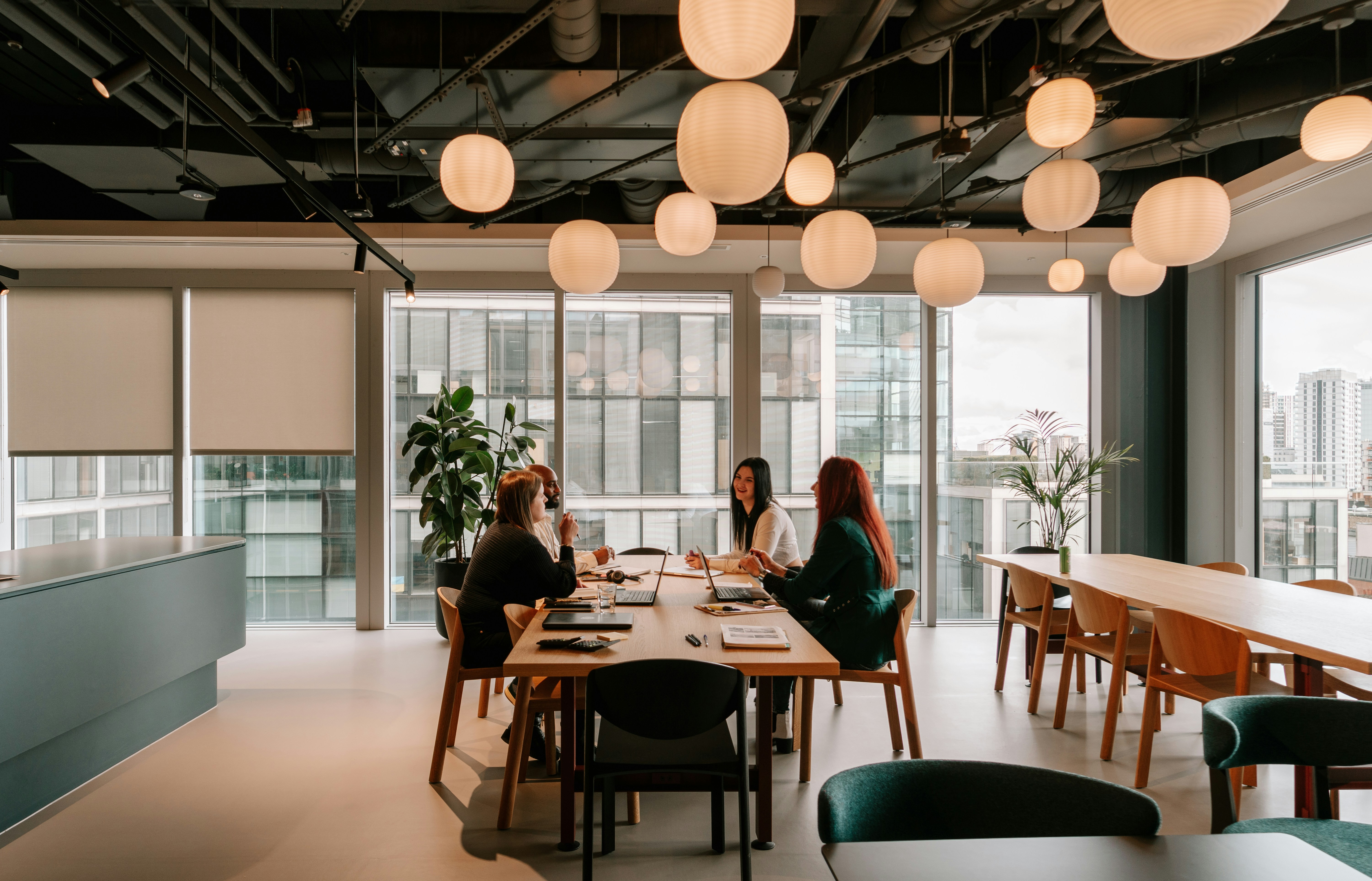 Three coworkers discussing documents at a conference table with a laptop in a sunlit office