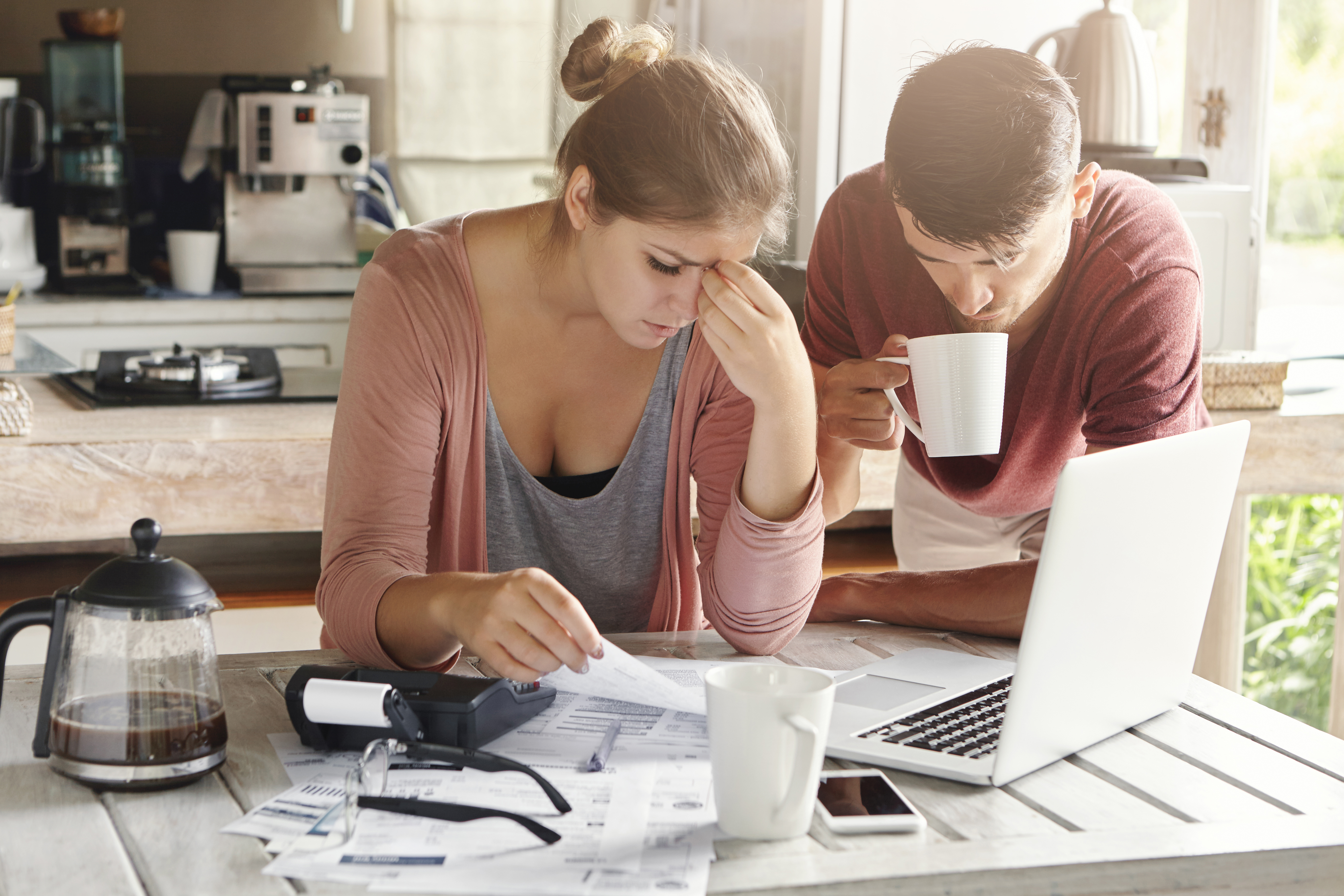 Couple reviewing financial documents at a kitchen table with a laptop and coffee.