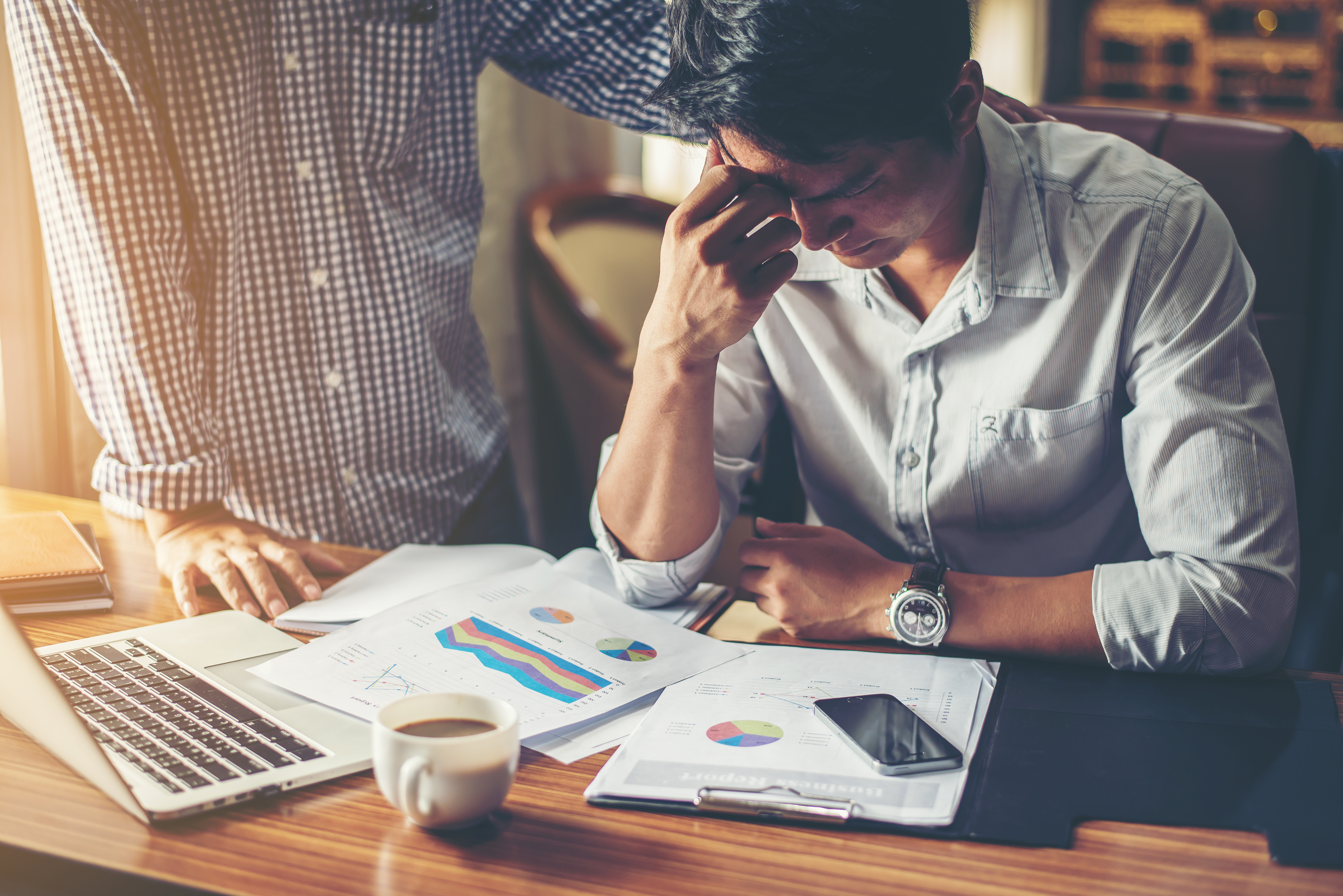 Stressed man sitting at desk with financial charts and laptop