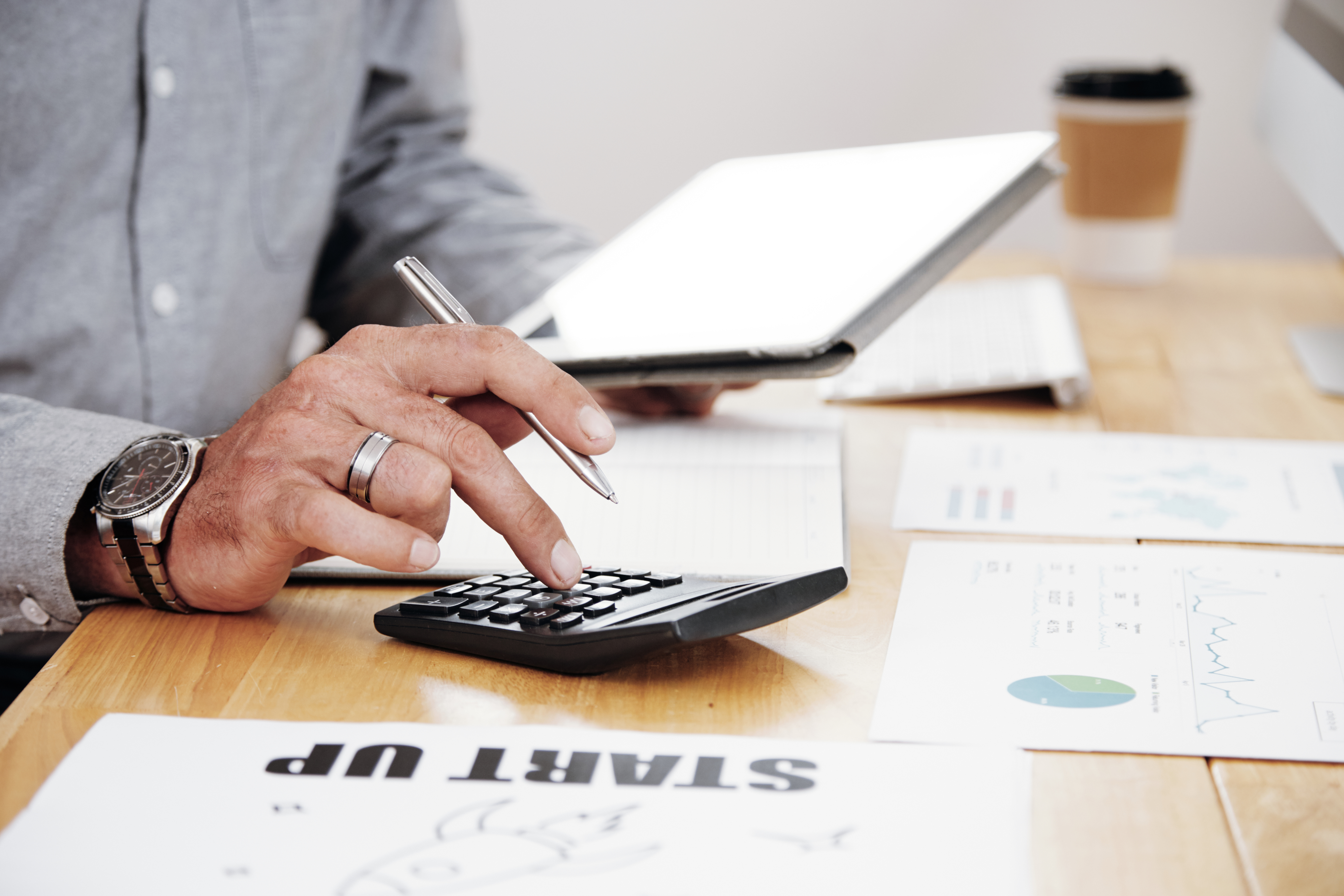 Person using a calculator and tablet at a desk with financial documents.