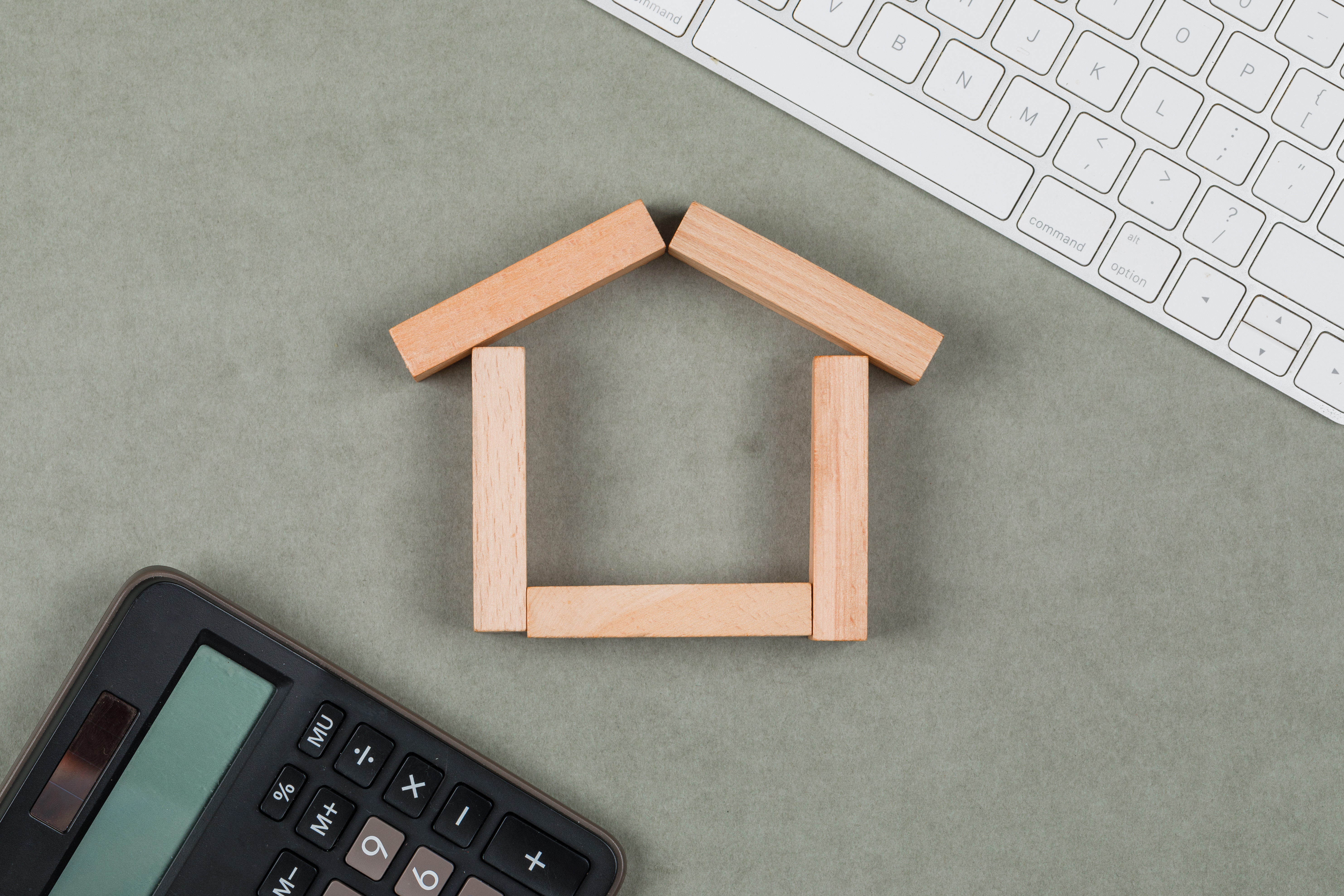 Wooden blocks forming a house shape next to a calculator and keyboard