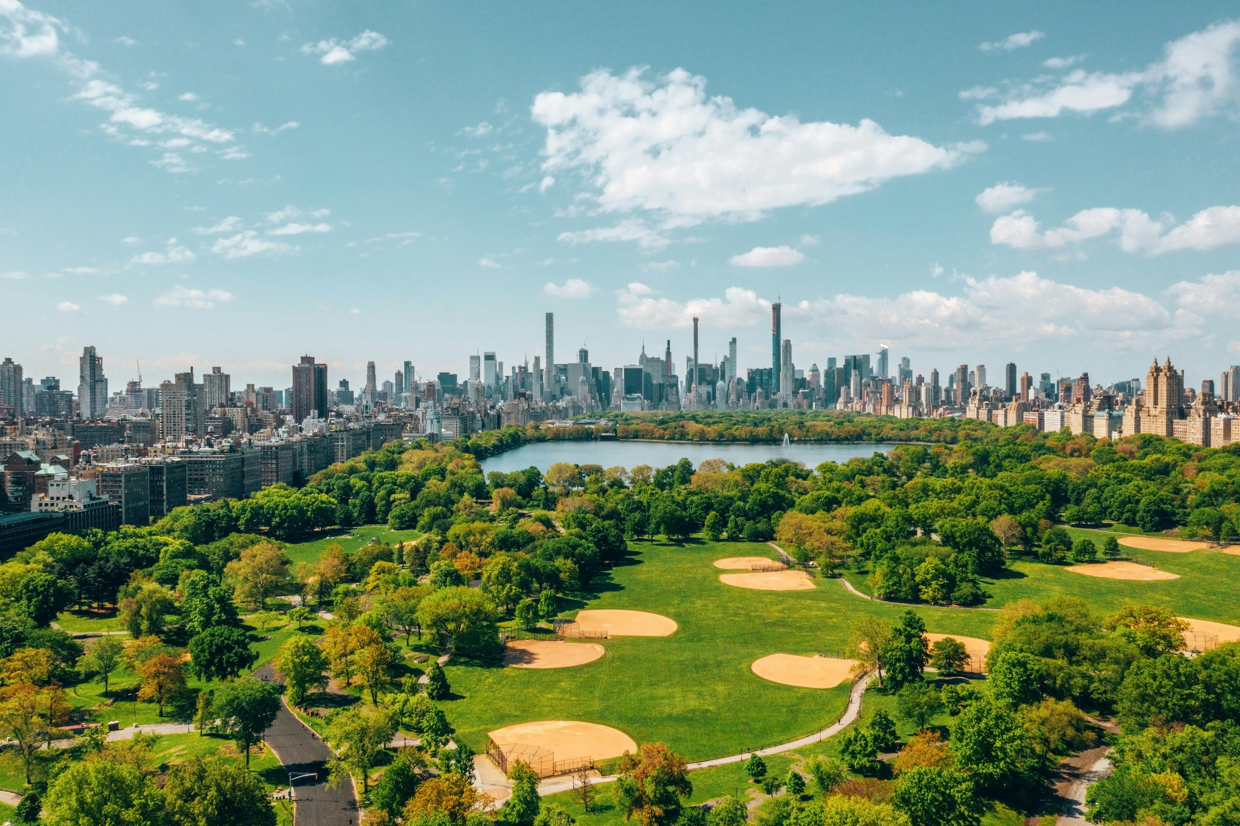 Aerial view of a large city park with green fields and a city skyline in the background