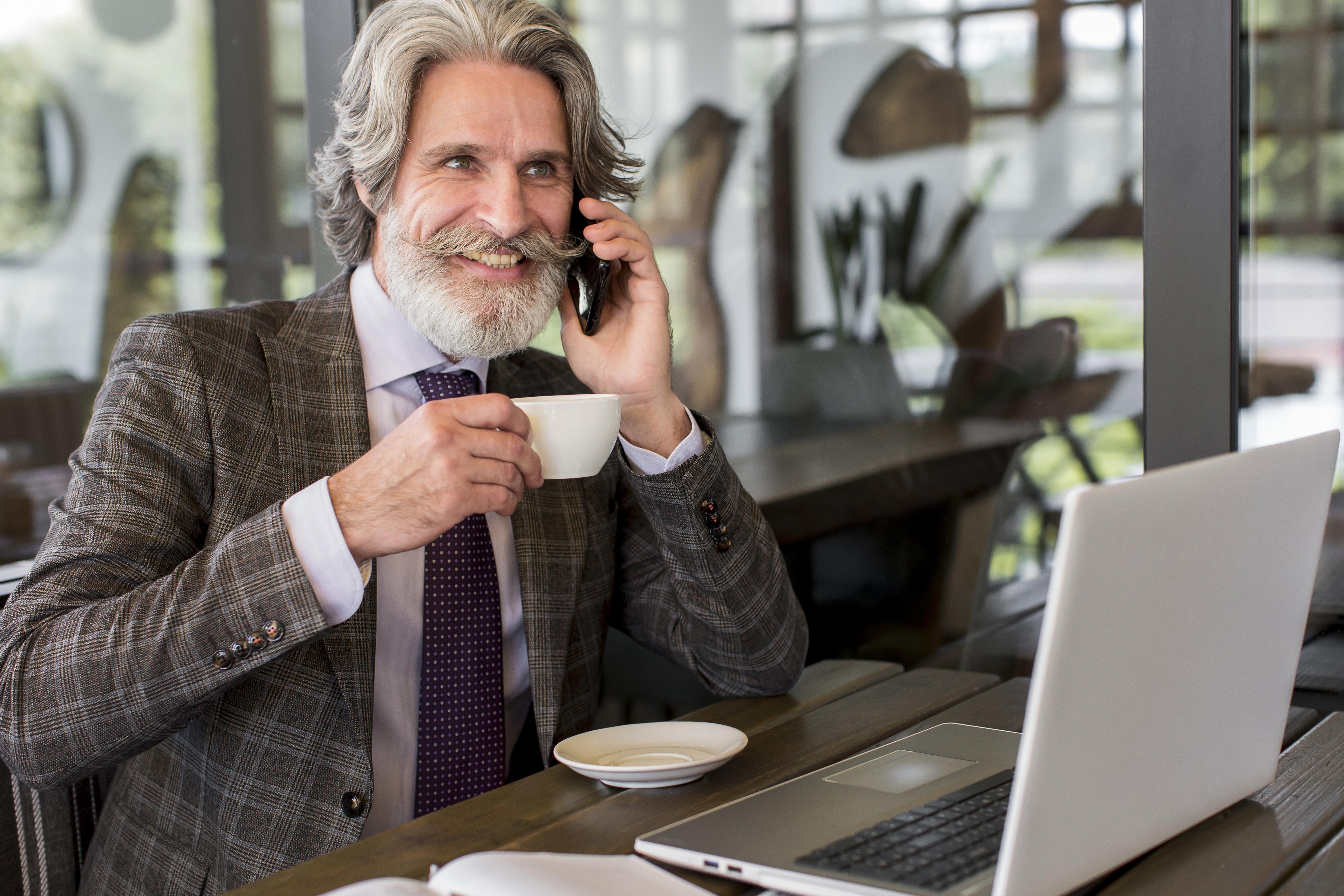 Smiling man with gray hair talking on phone while holding a coffee cup