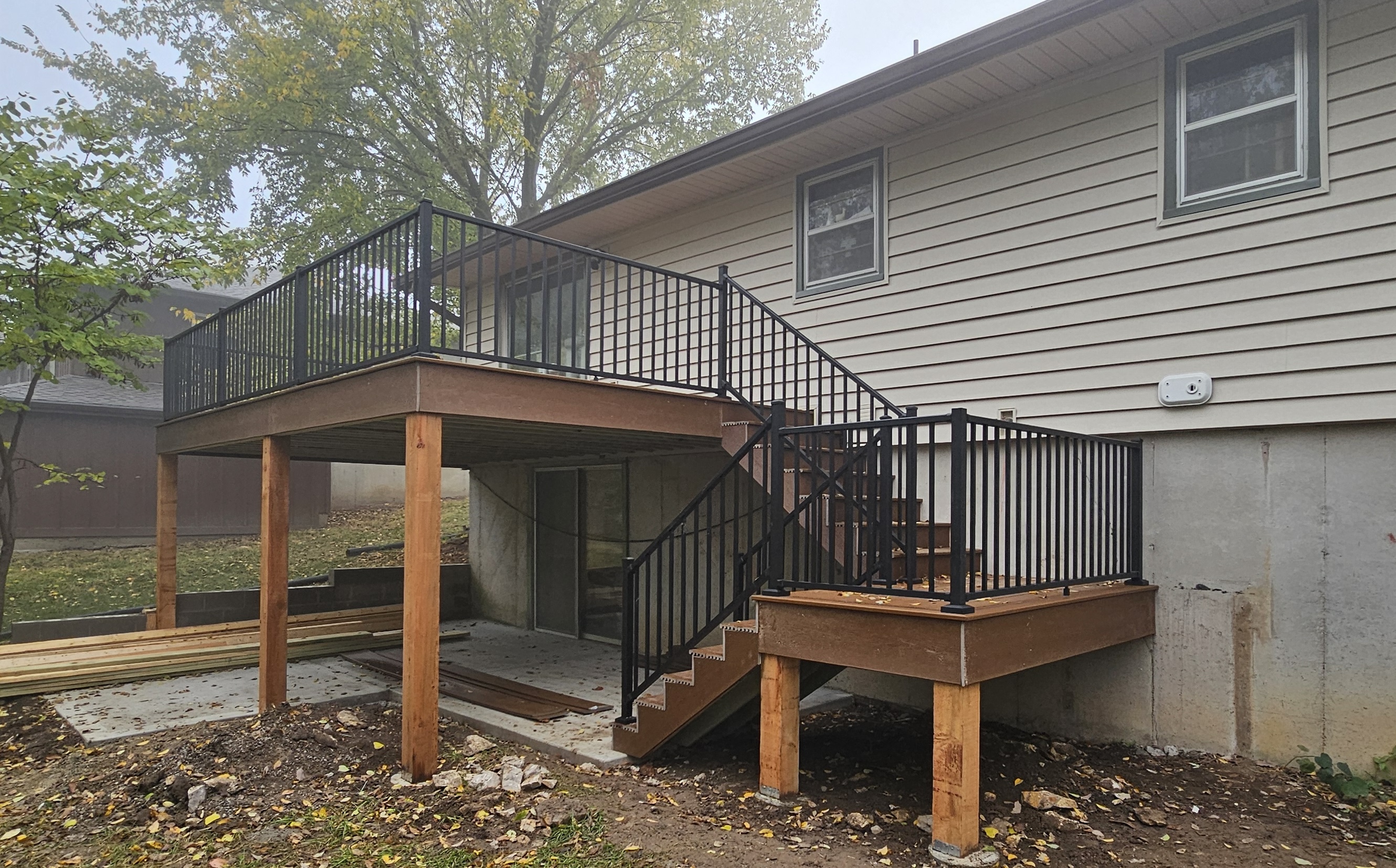 Backyard view of a house with a newly constructed wooden deck and black metal railings.