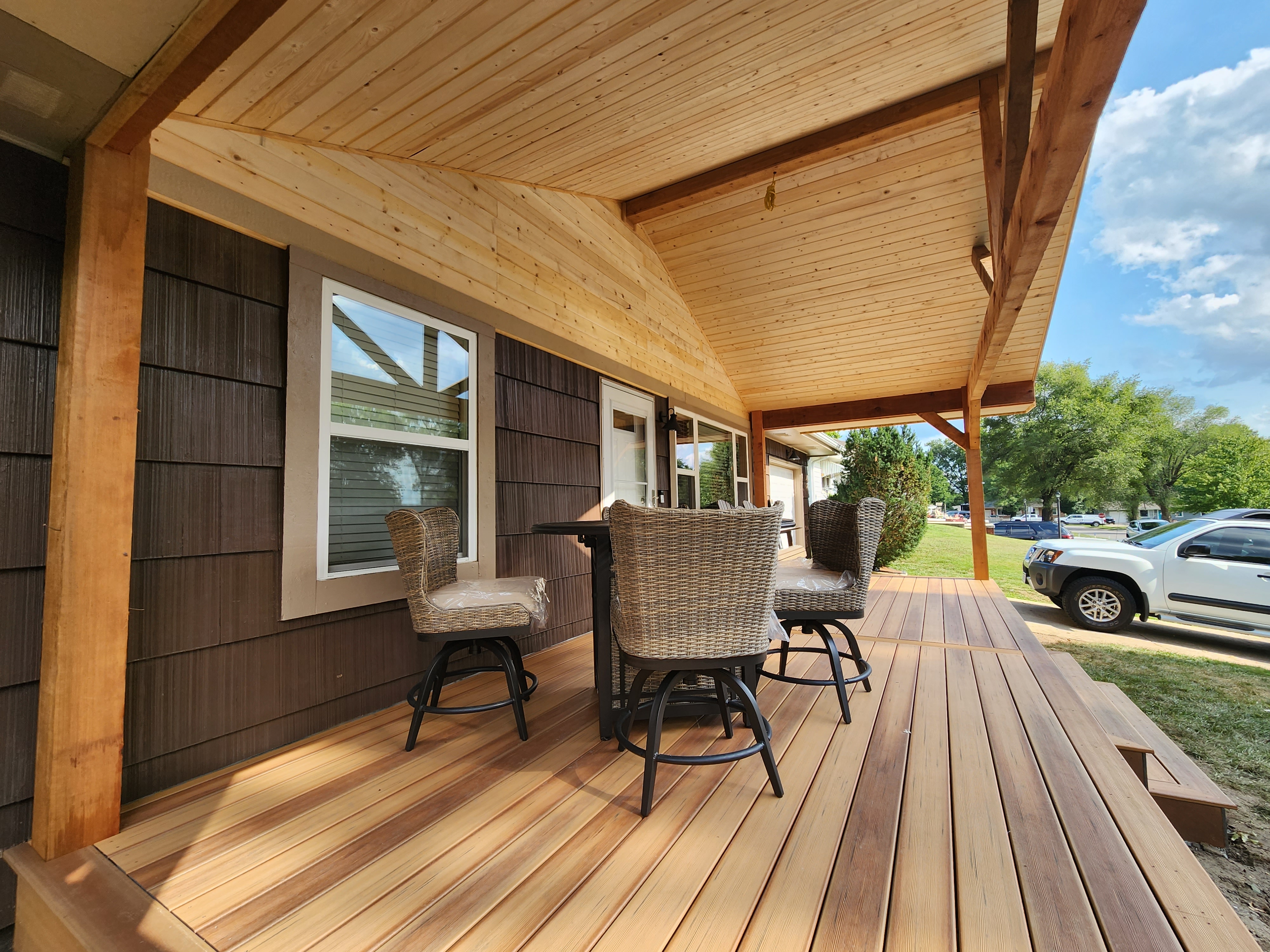 Wooden deck with wicker chairs and table under a covered porch
