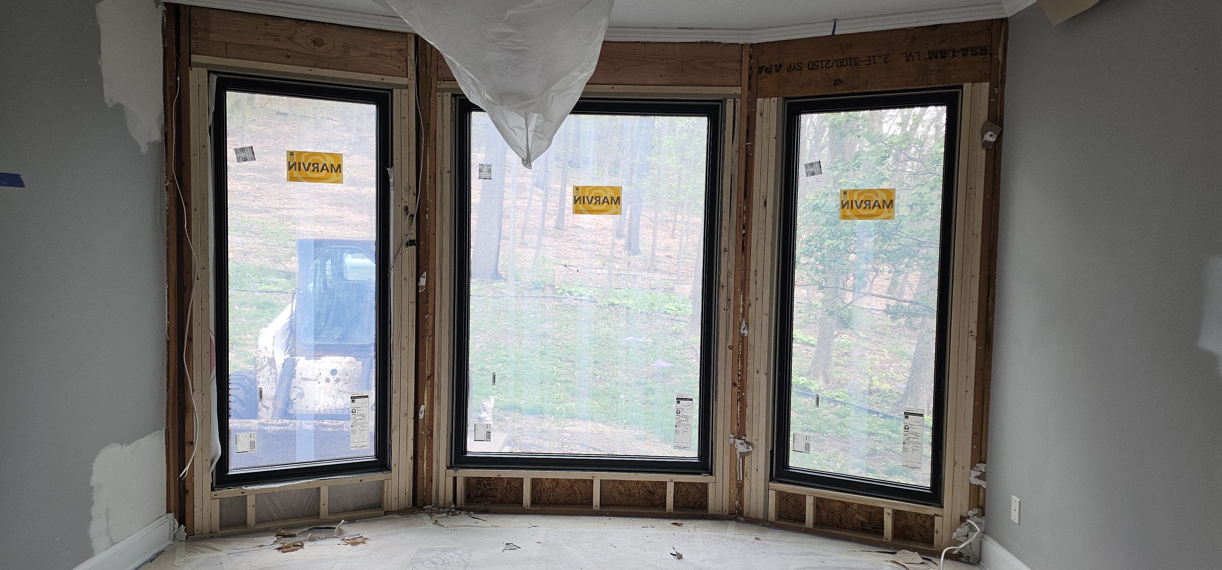 Room with three large windows under construction, overlooking a wooded area